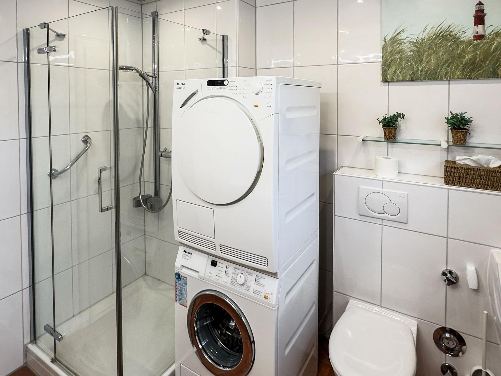 Badezimmer mit Dusche, Waschmaschine und Trockner. Wandbild mit Leuchtturm.