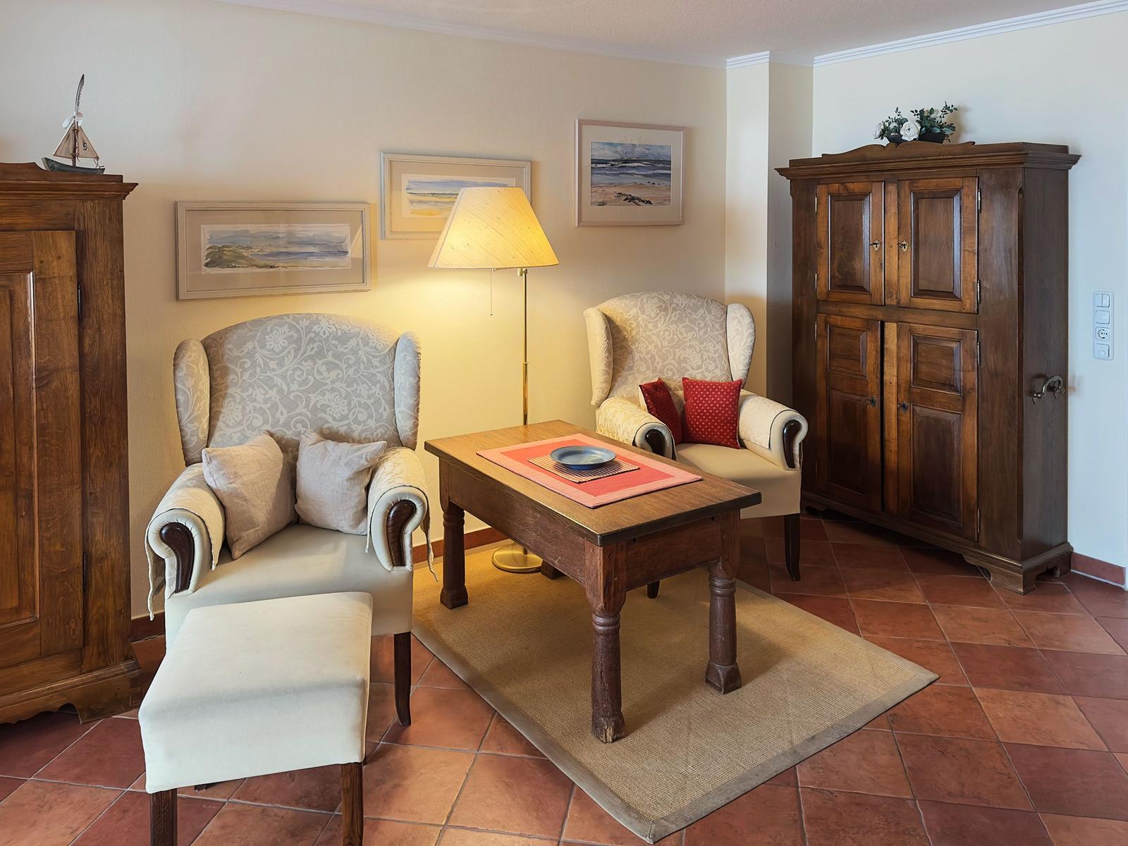 Zwei Sessel, Tisch, Stehlampe und zwei Schränke im Wohnzimmer mit Terrakottaboden.