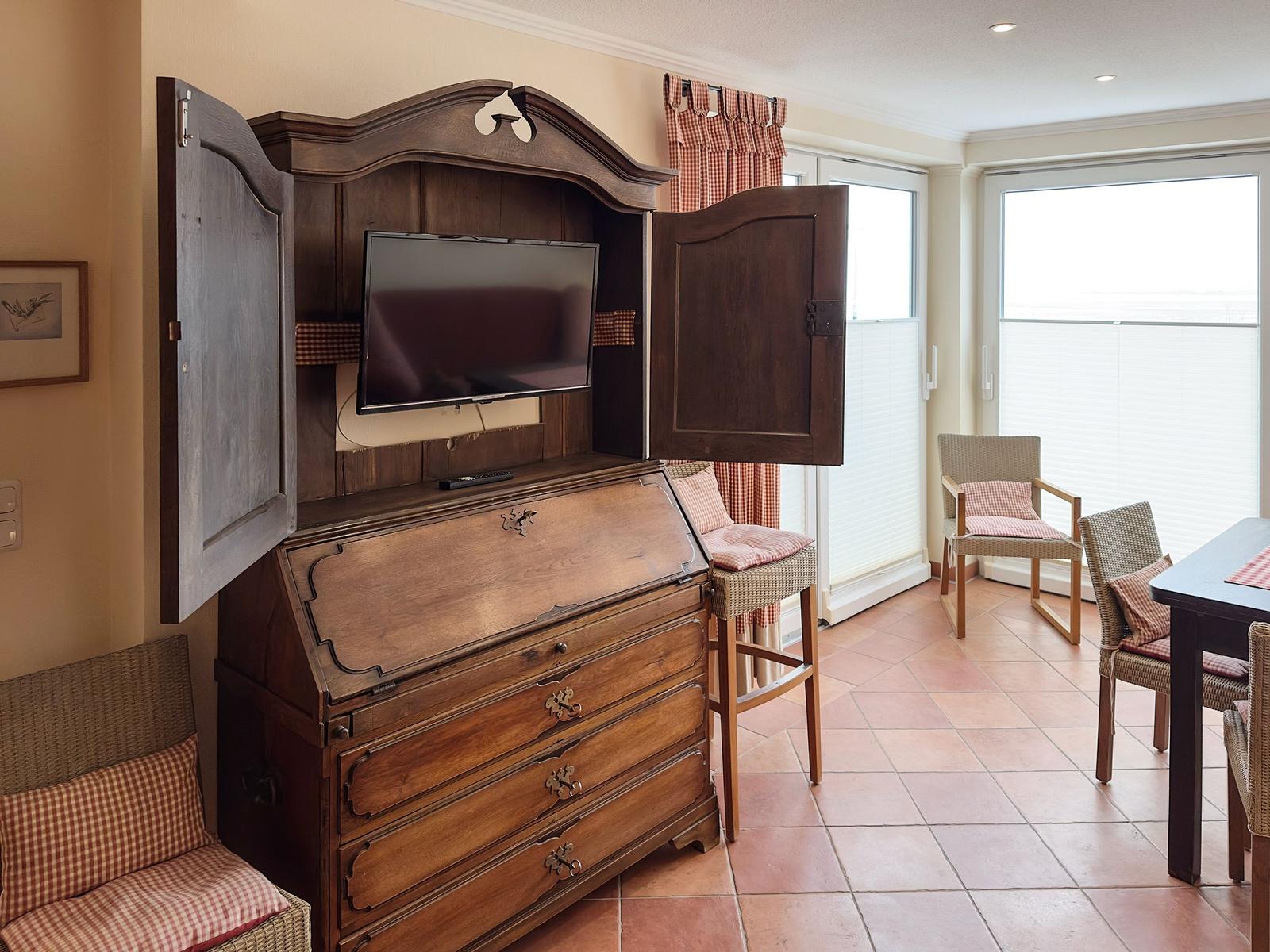 Holzschrank mit Fernseher, Sitzgelegenheiten und Fenster mit Jalousien.