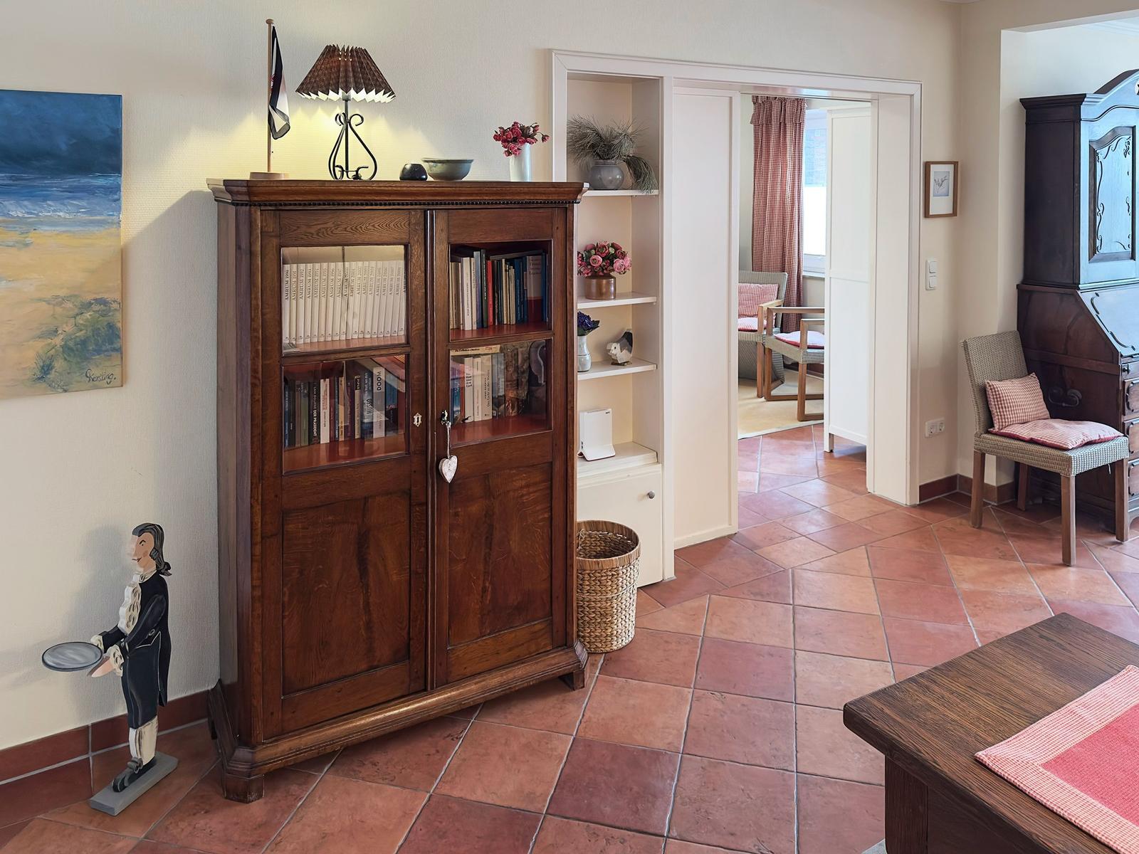 Ein Raum mit Holzschrank, Bücherregal und Terrakottaboden. Durchgang zu einem anderen Raum.