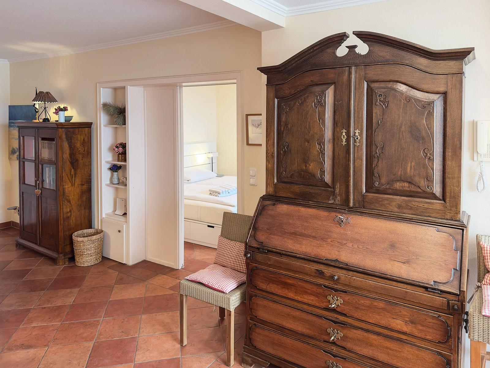 Ein Raum mit einem großen antiken Schrank und einem Blick in das Schlafzimmer.