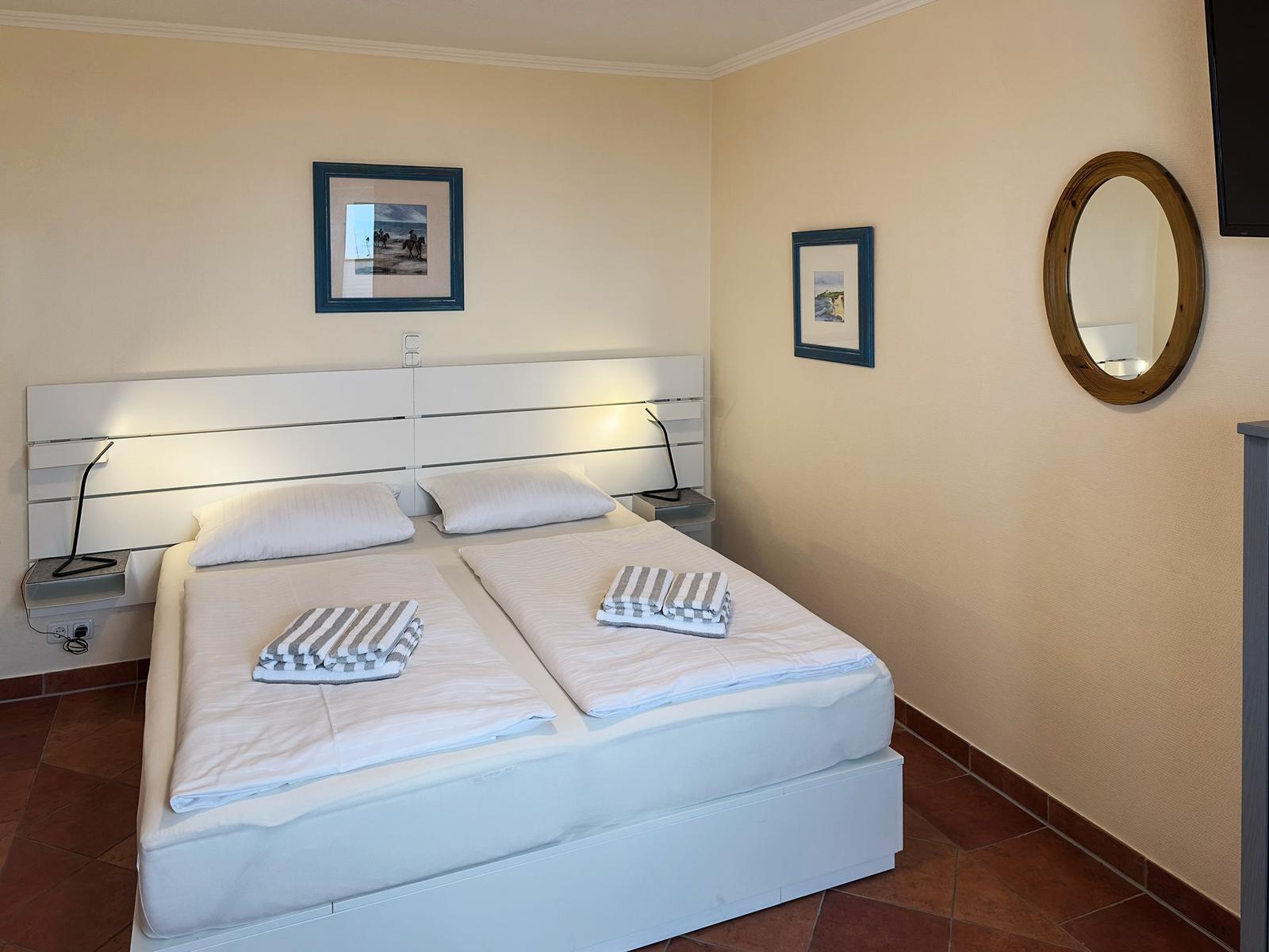 Ein Schlafzimmer mit Doppelbett, zwei Nachttischen und Wandbildern.
