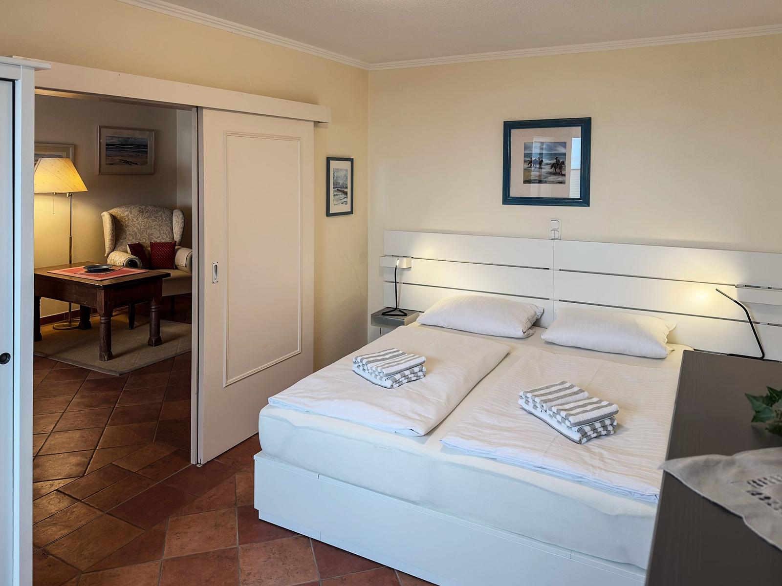 Schlafzimmer mit Doppelbett, Bettwäsche und Blick in Wohnbereich.
