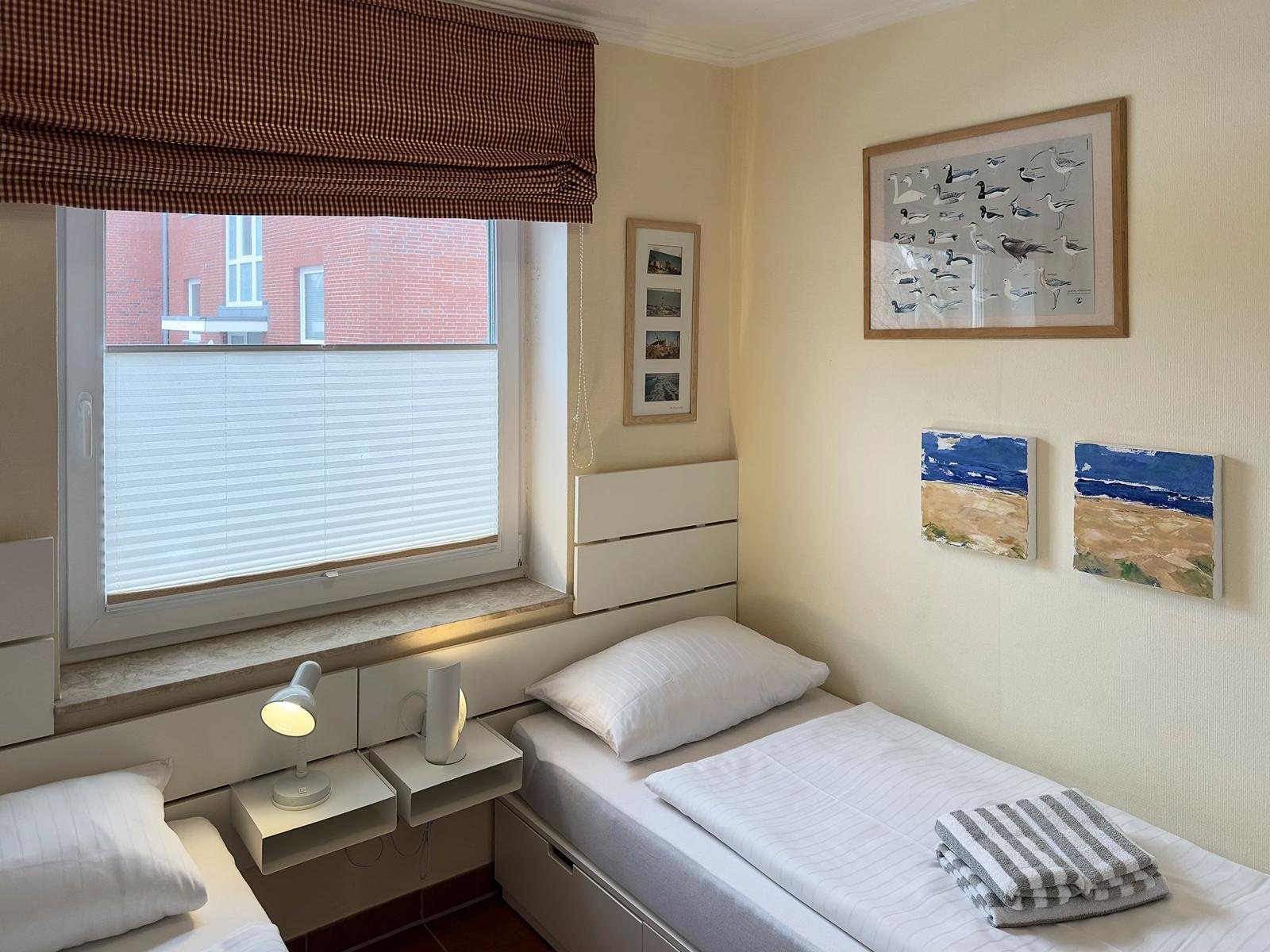 Zimmer mit zwei Betten, Fenster mit Jalousie und Wandbildern