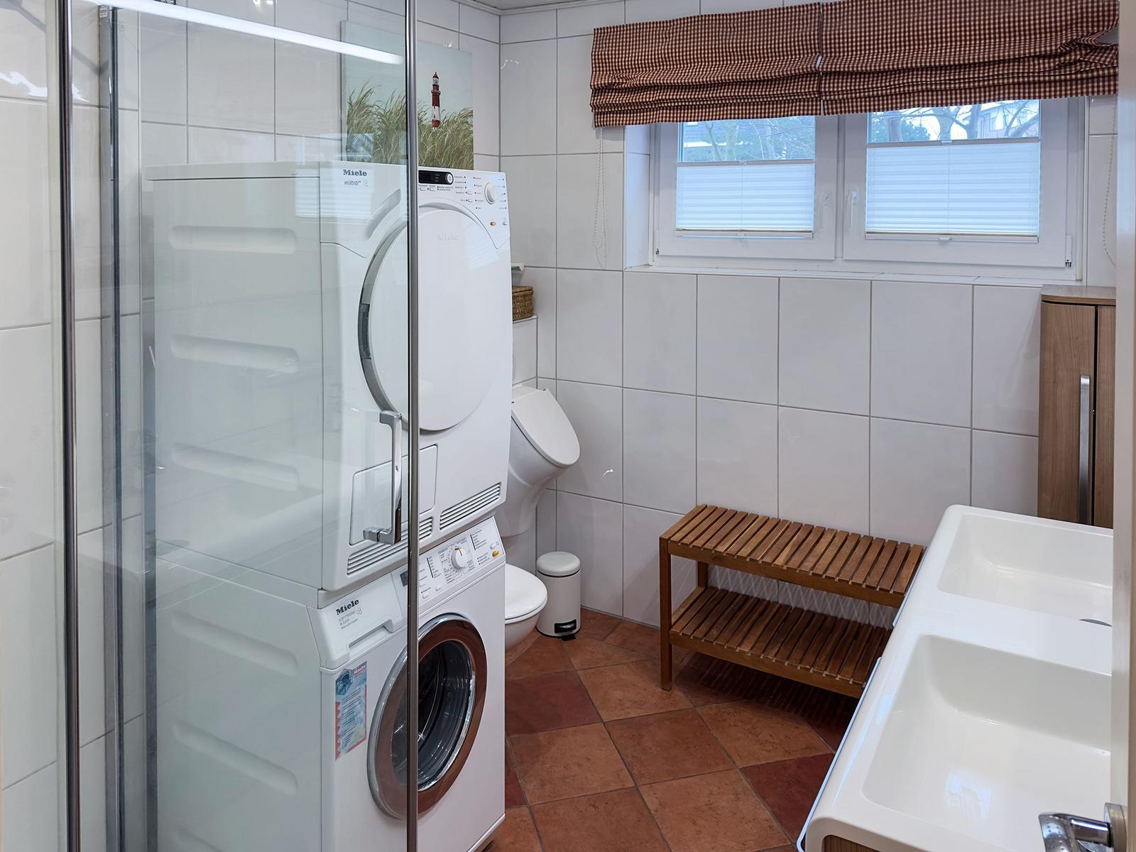 Waschmaschine und Trockner in Bad mit Waschbecken und Holzbank.