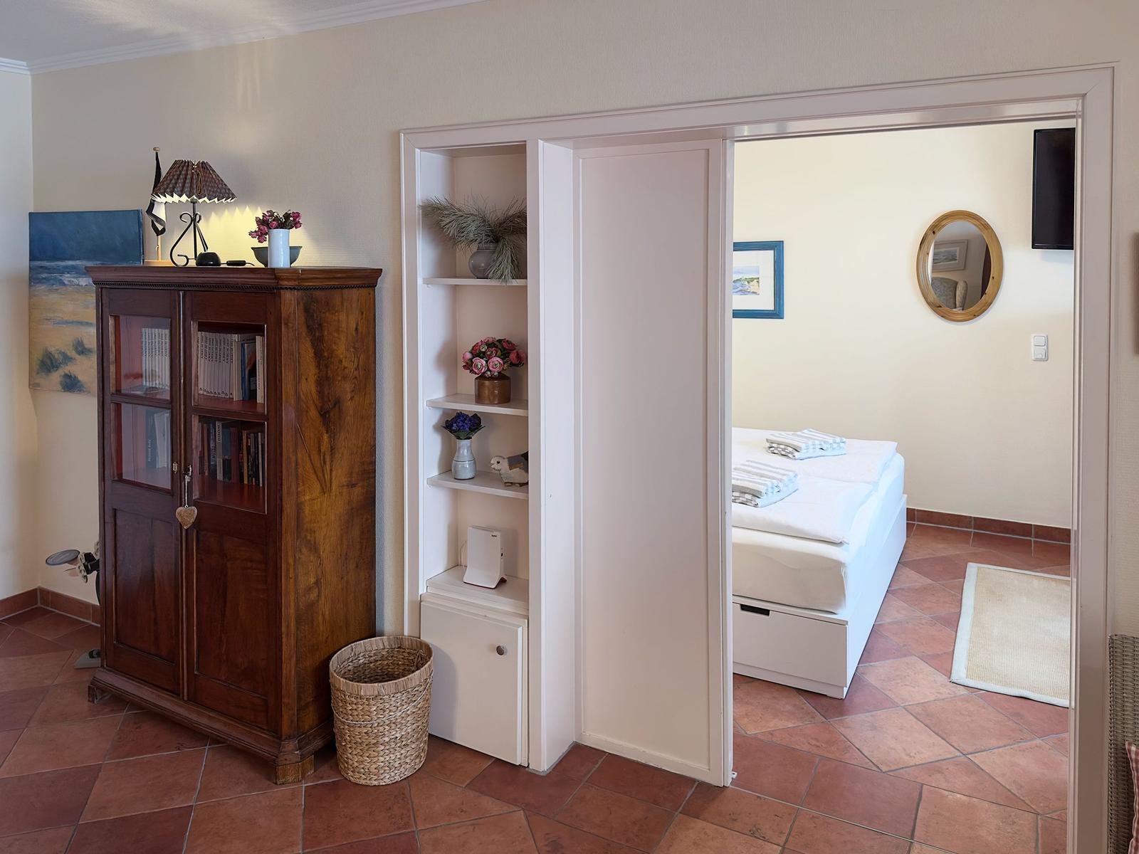 Ein Raum mit Holzschrank und Regal, Tür zum Schlafzimmer mit Bett und Spiegel.