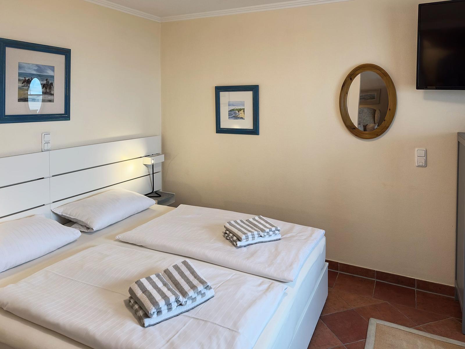 Schlafzimmer mit Doppelbett, zwei Handtüchern, Wandspiegel und Fernseher.