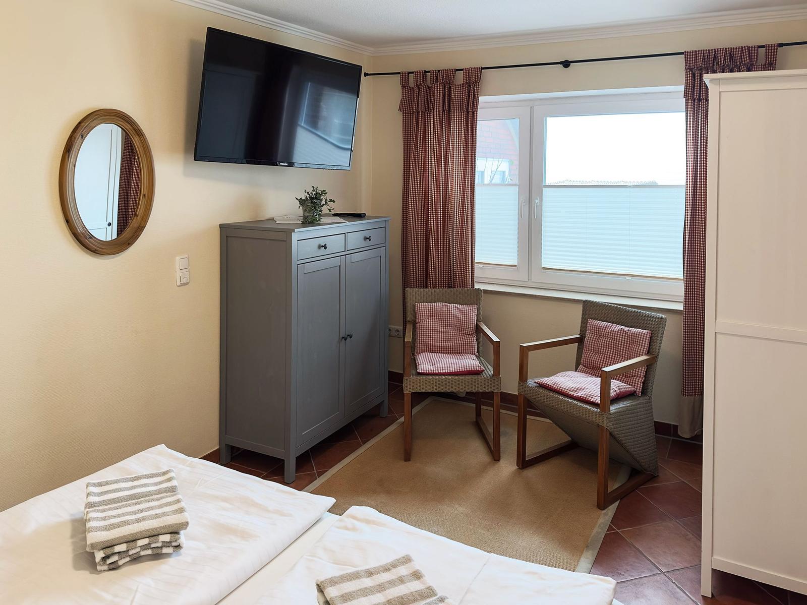 Zimmer mit Bett, Fernseher, Schrank und zwei Stühlen vor Fenster.