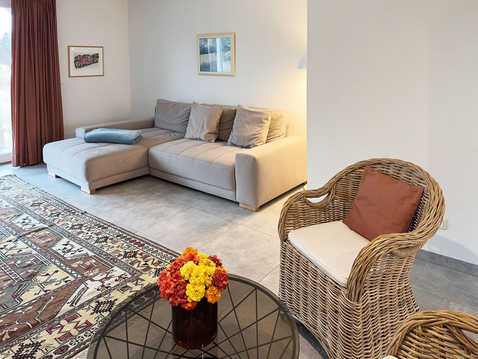 Wohnzimmer mit Eckcouch, Rattan-Stuhl und orientalischem Teppich.