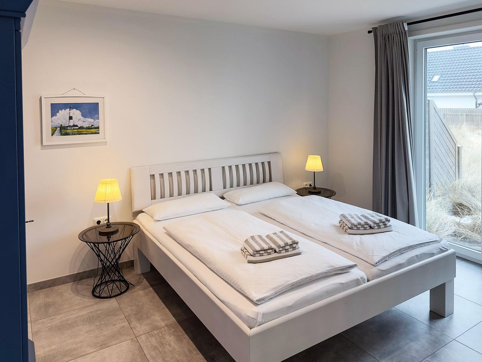 Schlafzimmer mit Doppelbett, zwei Nachttischen und Fensterblick auf Garten.