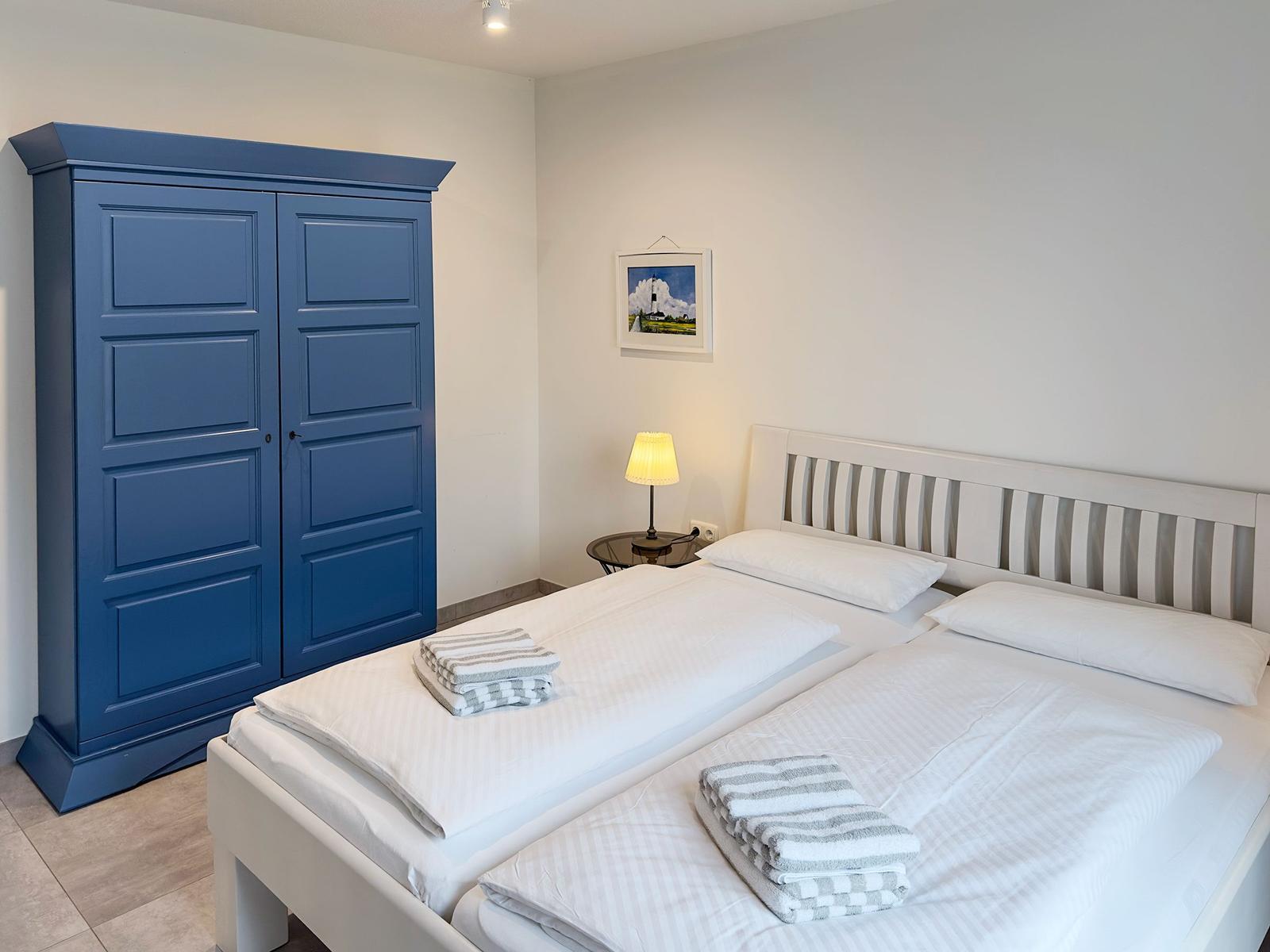 Schlafzimmer mit Doppelbett, blauem Schrank und Nachttisch mit Lampe.