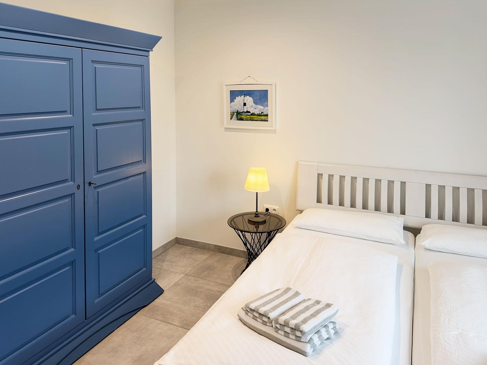 Zimmer mit Doppelbett, blauem Schrank und Nachttisch mit Lampe.