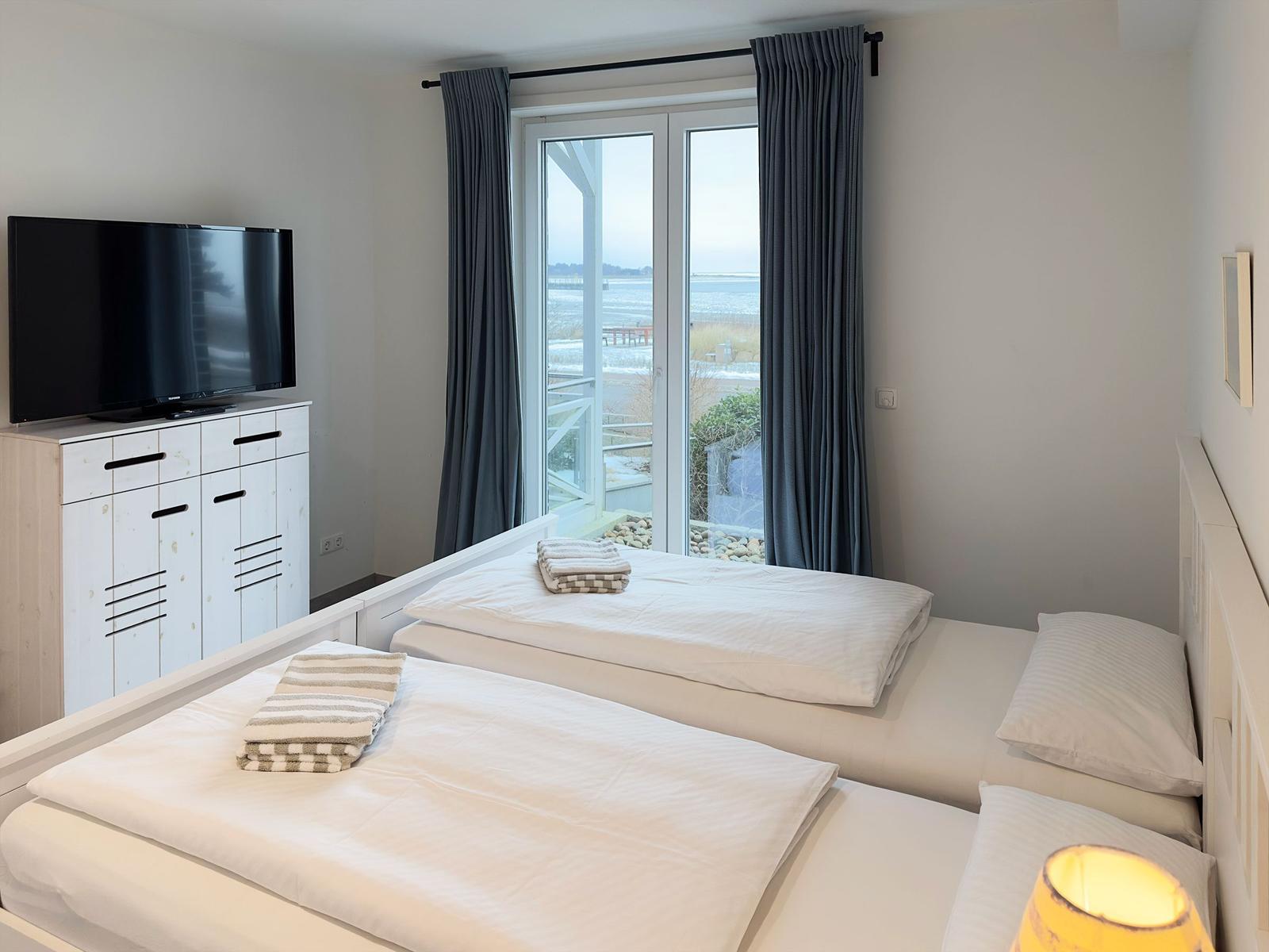 Zwei Betten mit weißen Bettwäschen, Fernseher und Fenster mit Blick aufs Wasser.