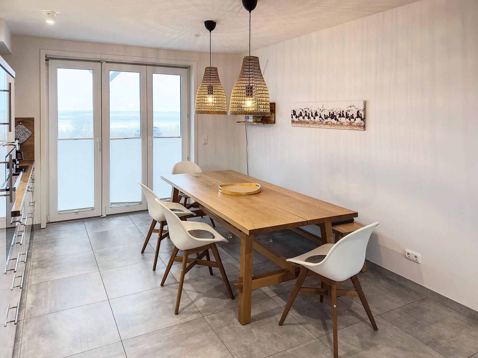 Essbereich mit Holztisch, weißen Stühlen und Blick aufs Meer.