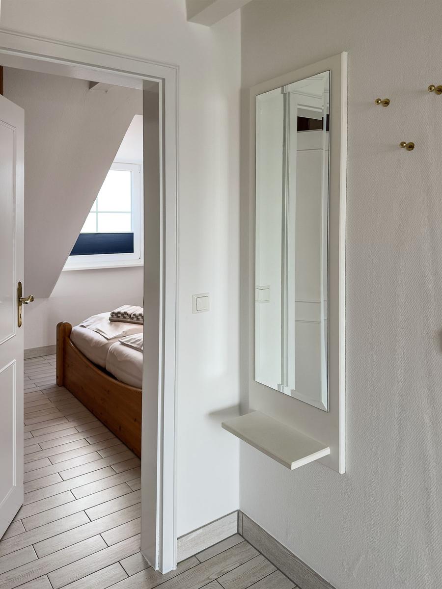 Schlafzimmer mit Holzbett und Dachfenster. Spiegel und Haken an der Wand.