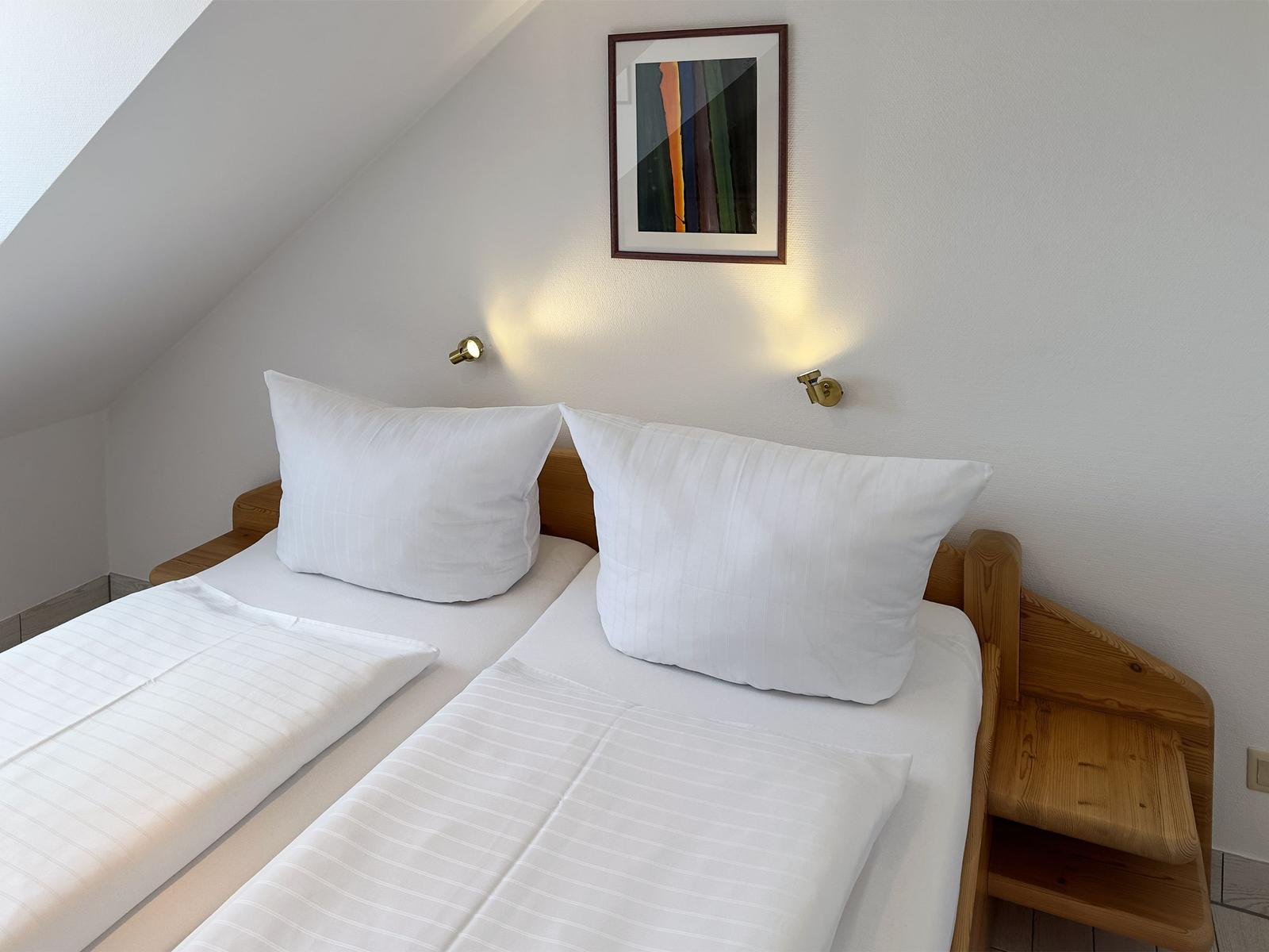 Ein Schlafzimmer mit Doppelbett, Holzgestell und Wandbild unter Dachschräge.