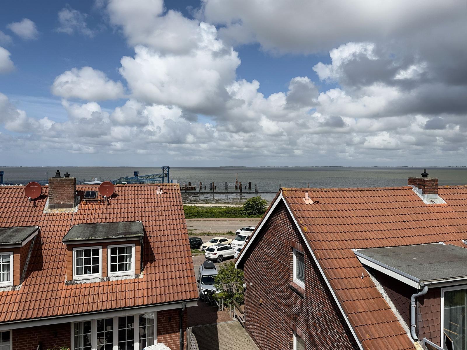 Roter Ziegeldachbereich mit Blick aufs Wasser und Himmel mit Wolken.