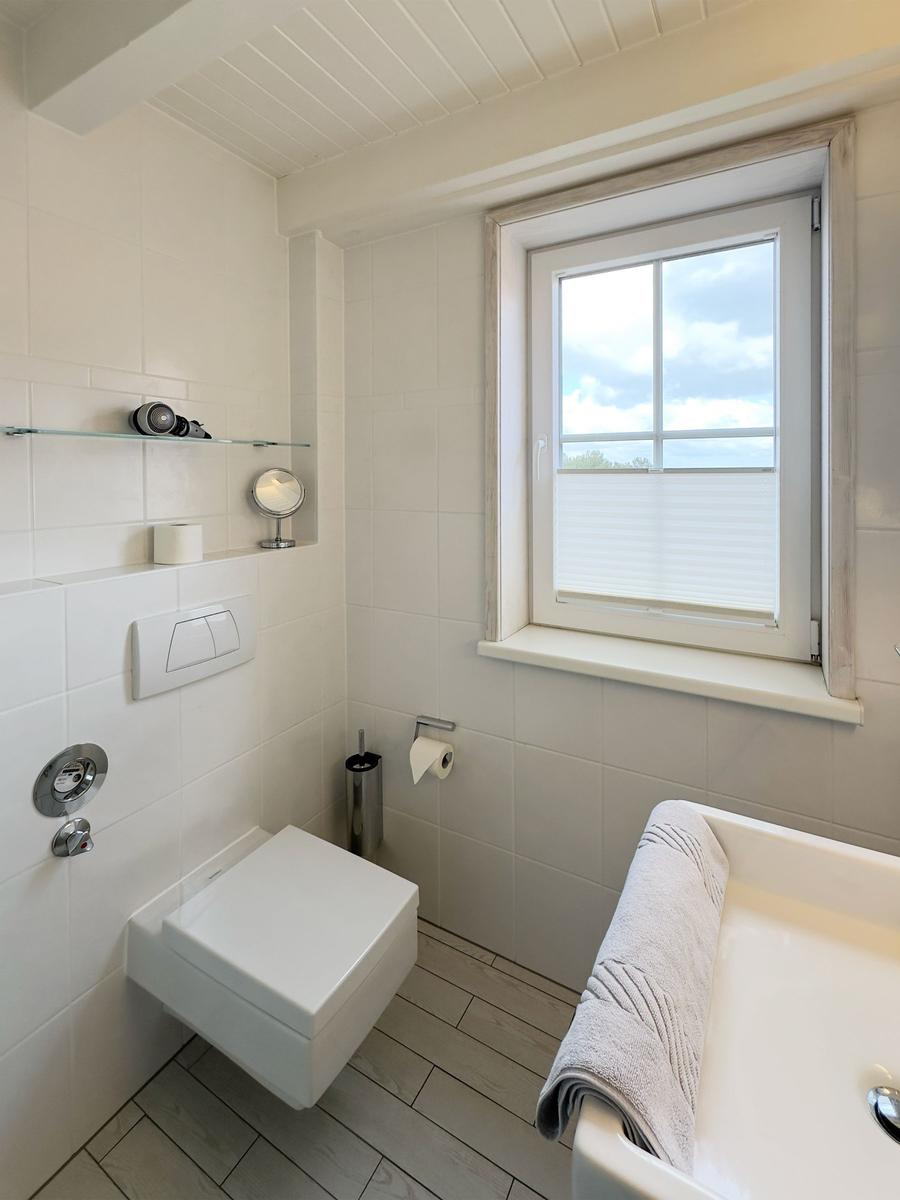 Badezimmer mit Toilette, Waschbecken und Fenster mit Blick nach draußen.
