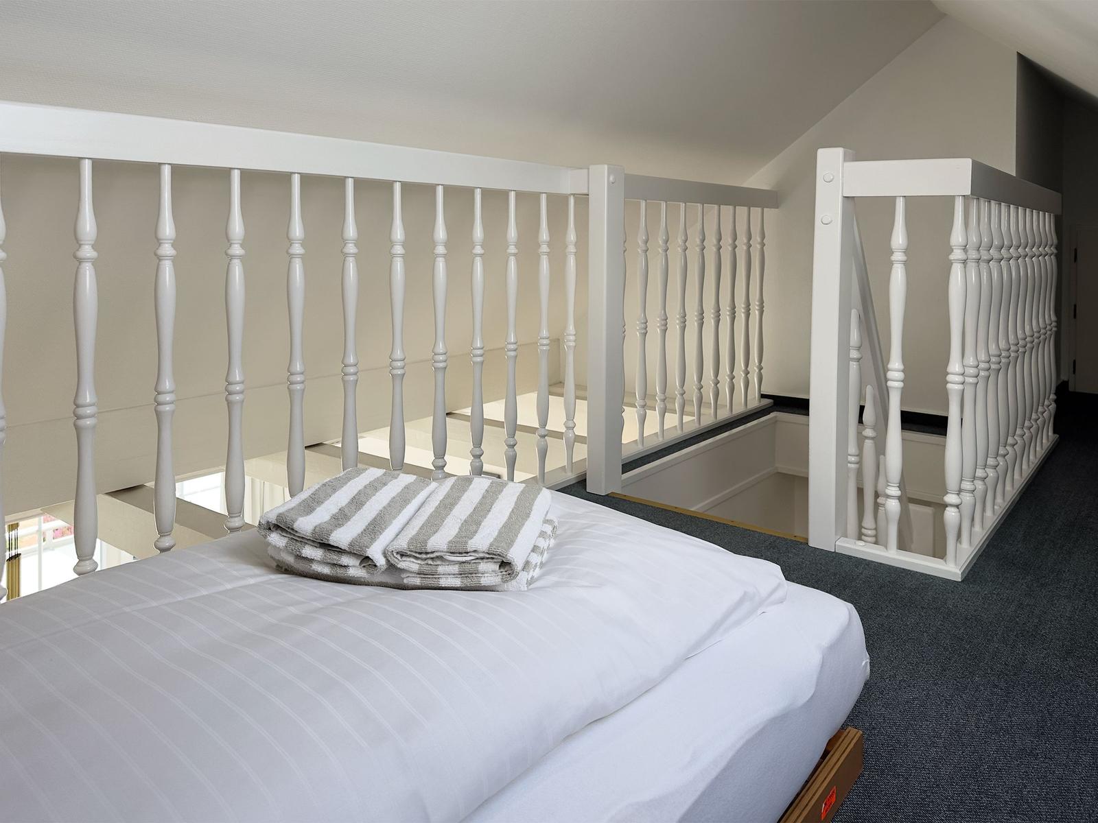 Schlafzimmer mit weißer Matratze, gestreifter Bettwäsche und weißer Geländerstruktur.