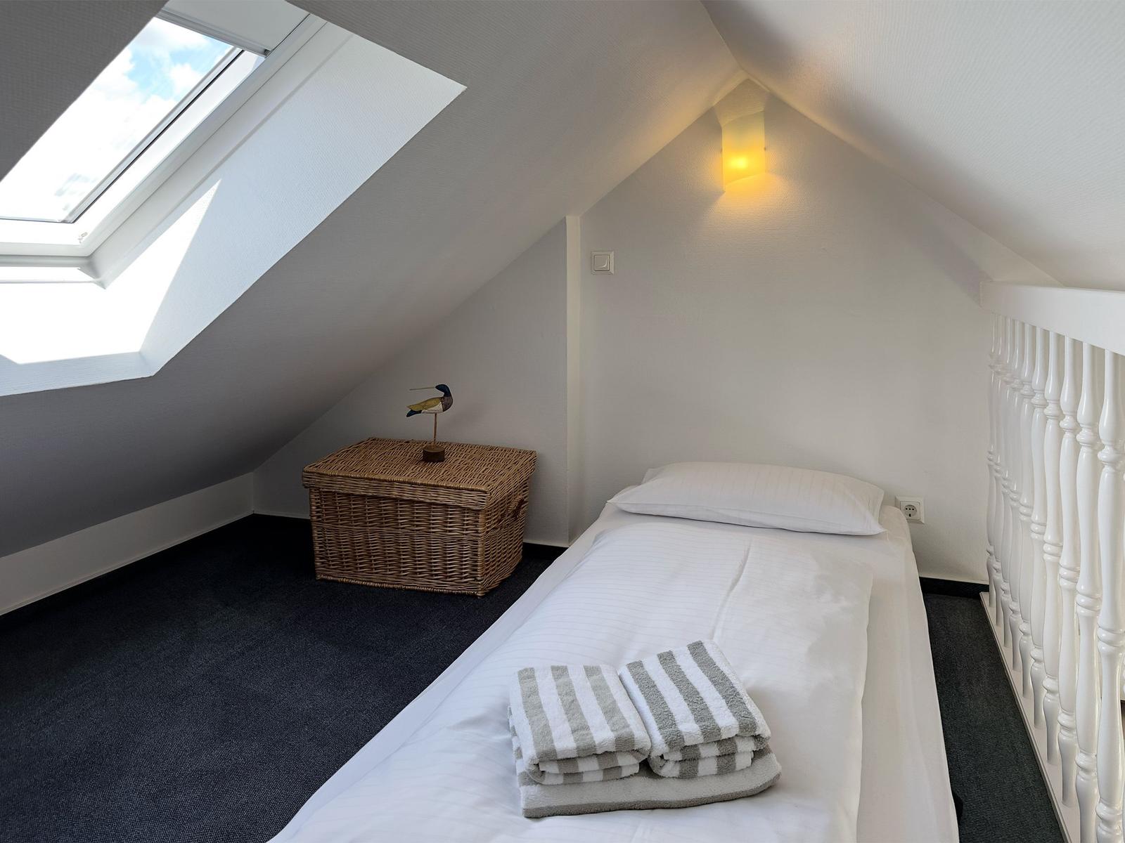 Dachgeschosszimmer mit Dachfenster, Bett und Korb.