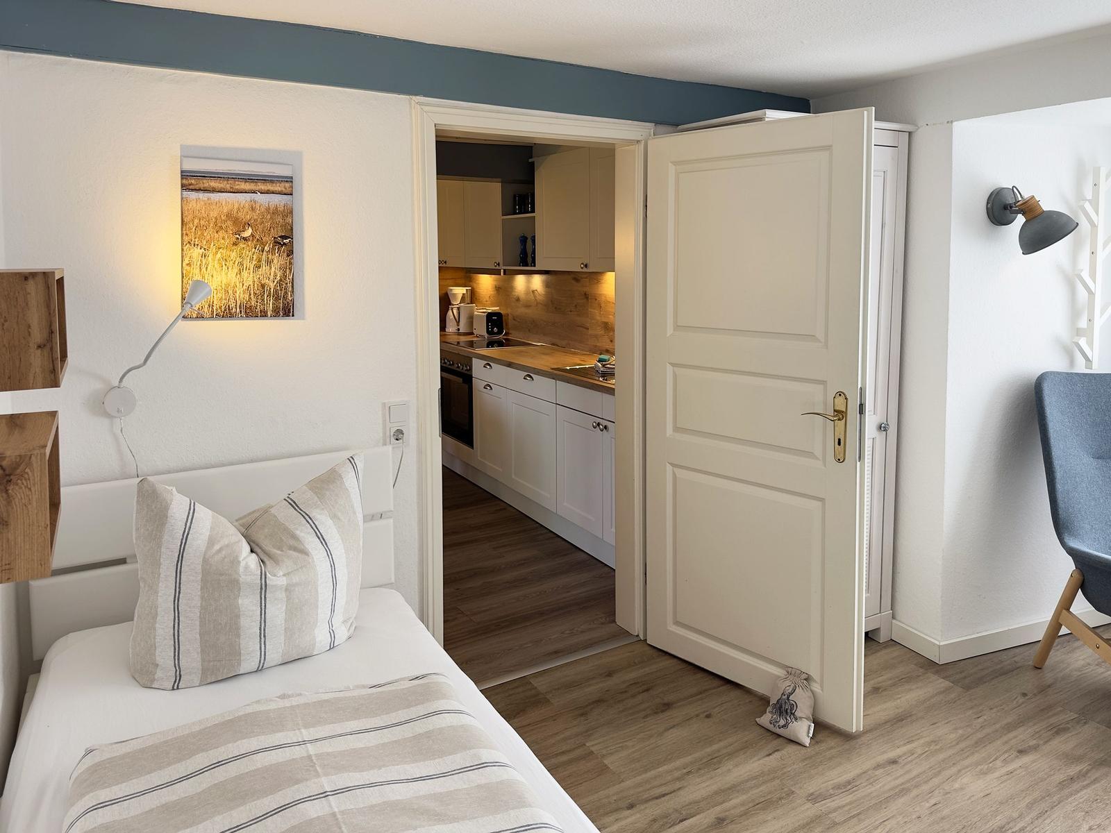 Schlafzimmer mit Bett, Wandbild und Tür zur Küche.