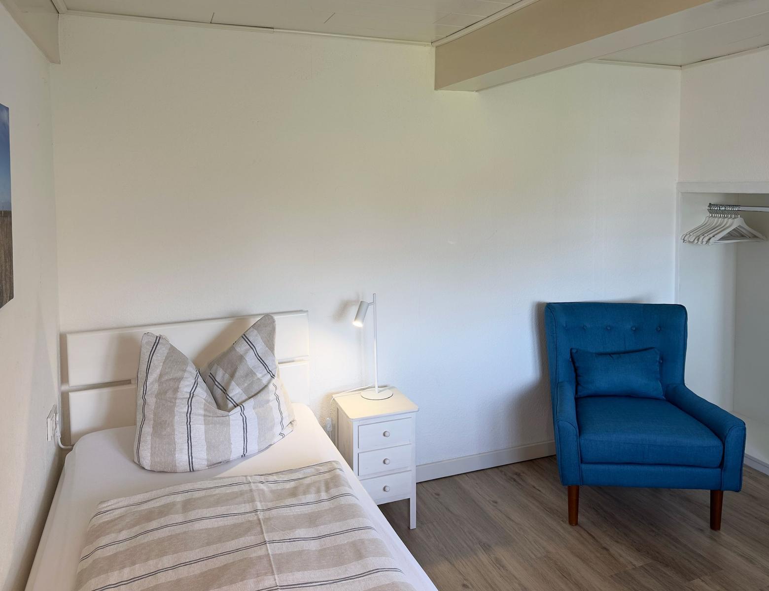 Ein Schlafzimmer mit Bett, Nachttisch und blauer Sessel.
