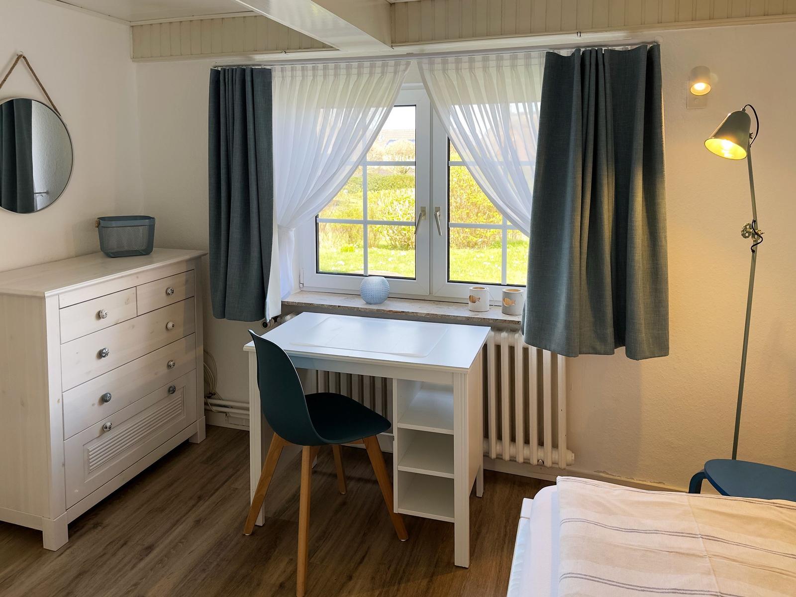 Schlafzimmer mit Schreibtisch, Bett und Fenster mit Blick auf Grünflächen.