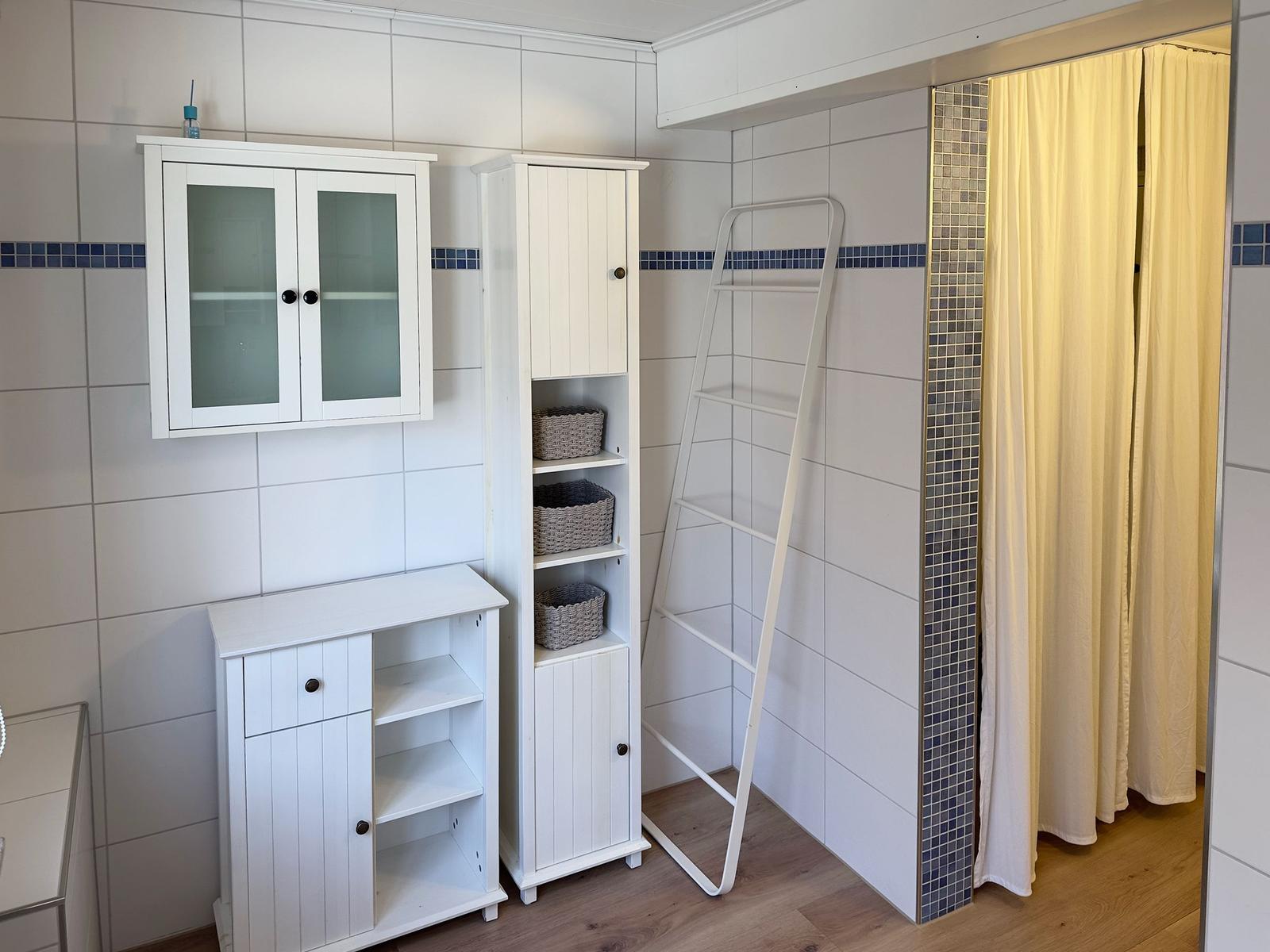 Badezimmer mit weißen Schränken, Duschvorhang und Handtuchhalter.