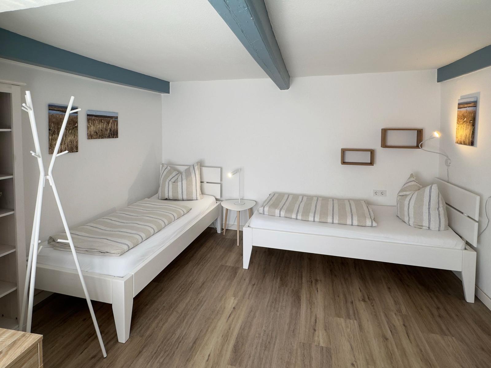 Zwei weiße Betten mit Streifenbetten, Holzboden und blaue Balken an der Decke.