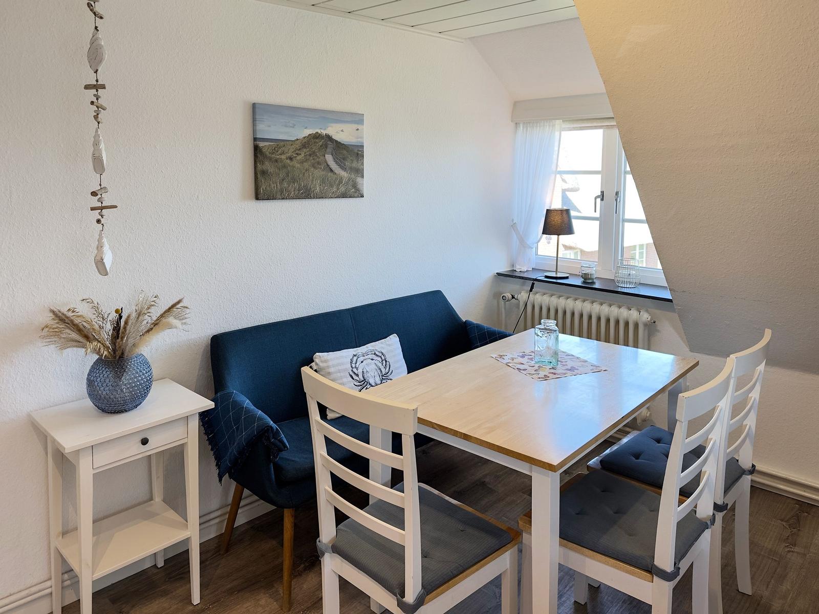 Essbereich mit Tisch, Stühlen und Sofa. Wandbild und Fenster sichtbar.