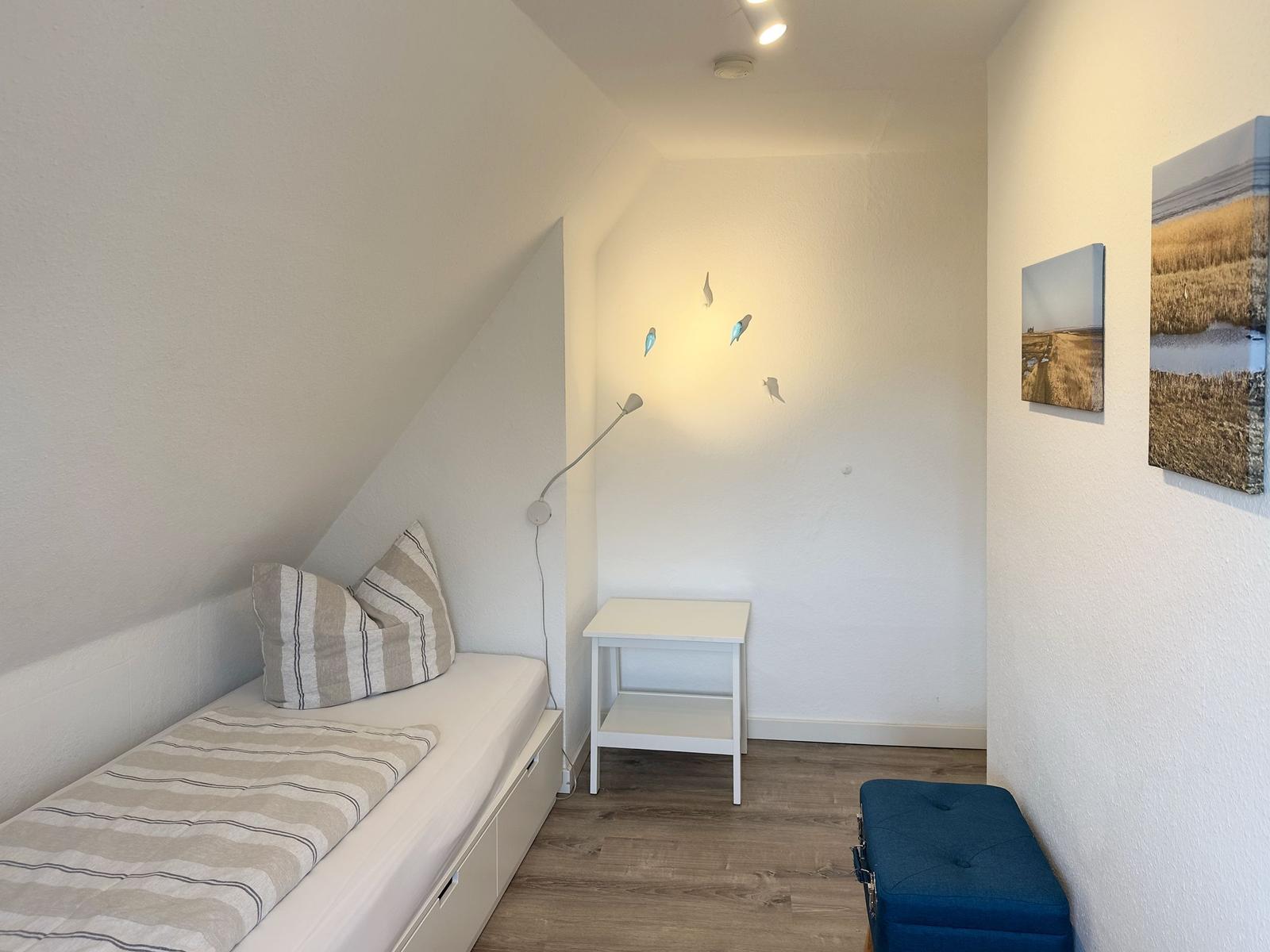 Schlafzimmer mit Bett, Tisch und Wandbildern.
