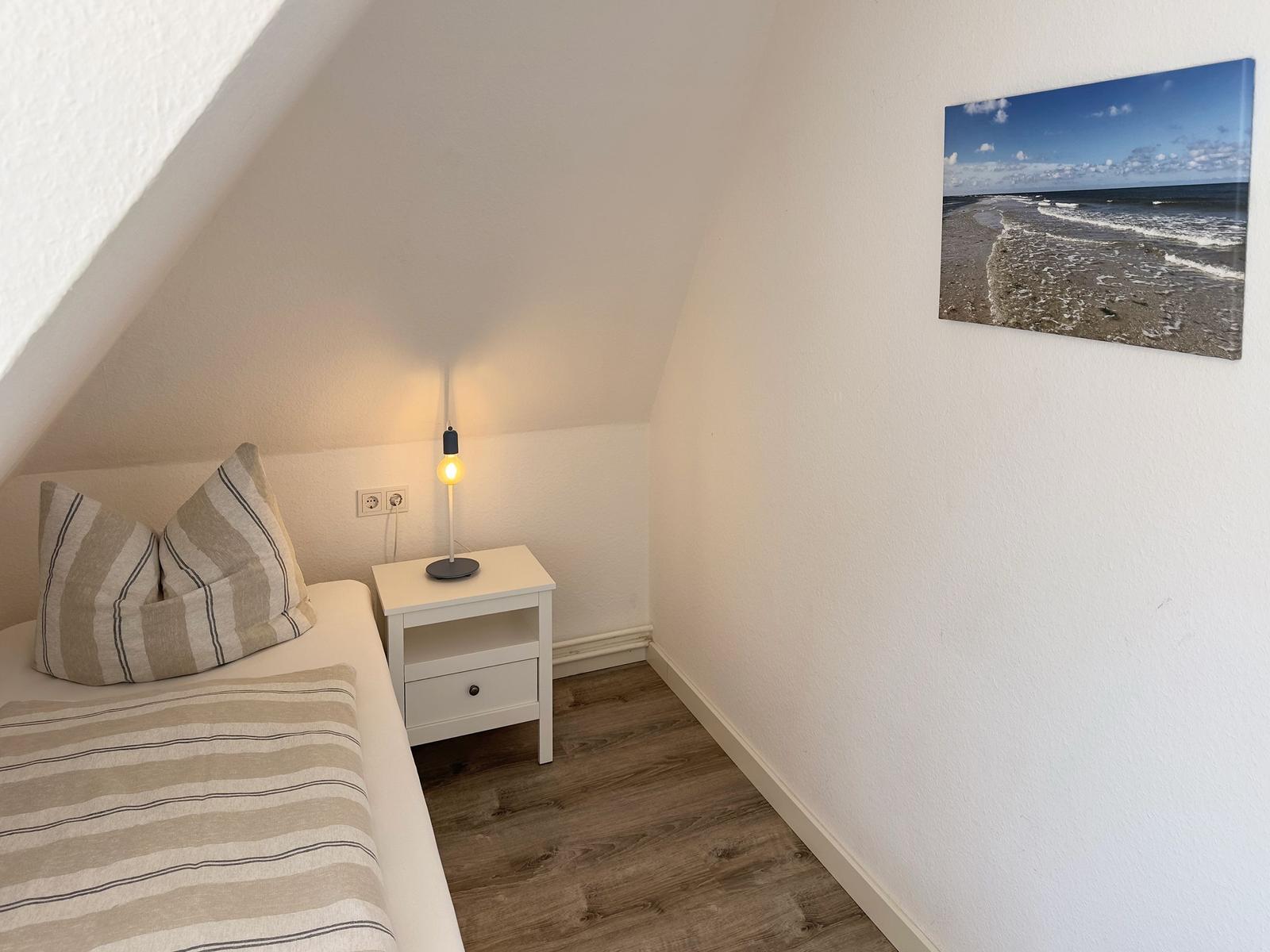 Schlafzimmer mit Dachschräge, Bett, Nachttisch und Strandbild an der Wand.