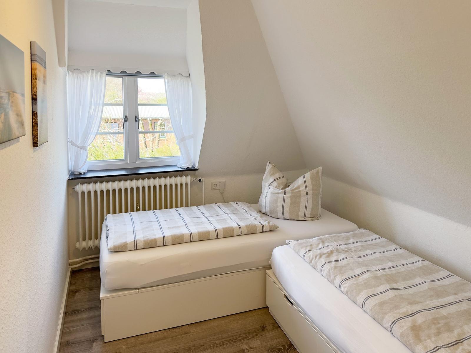 Zimmer mit zwei Einzelbetten, Fenster und Heizkörper.