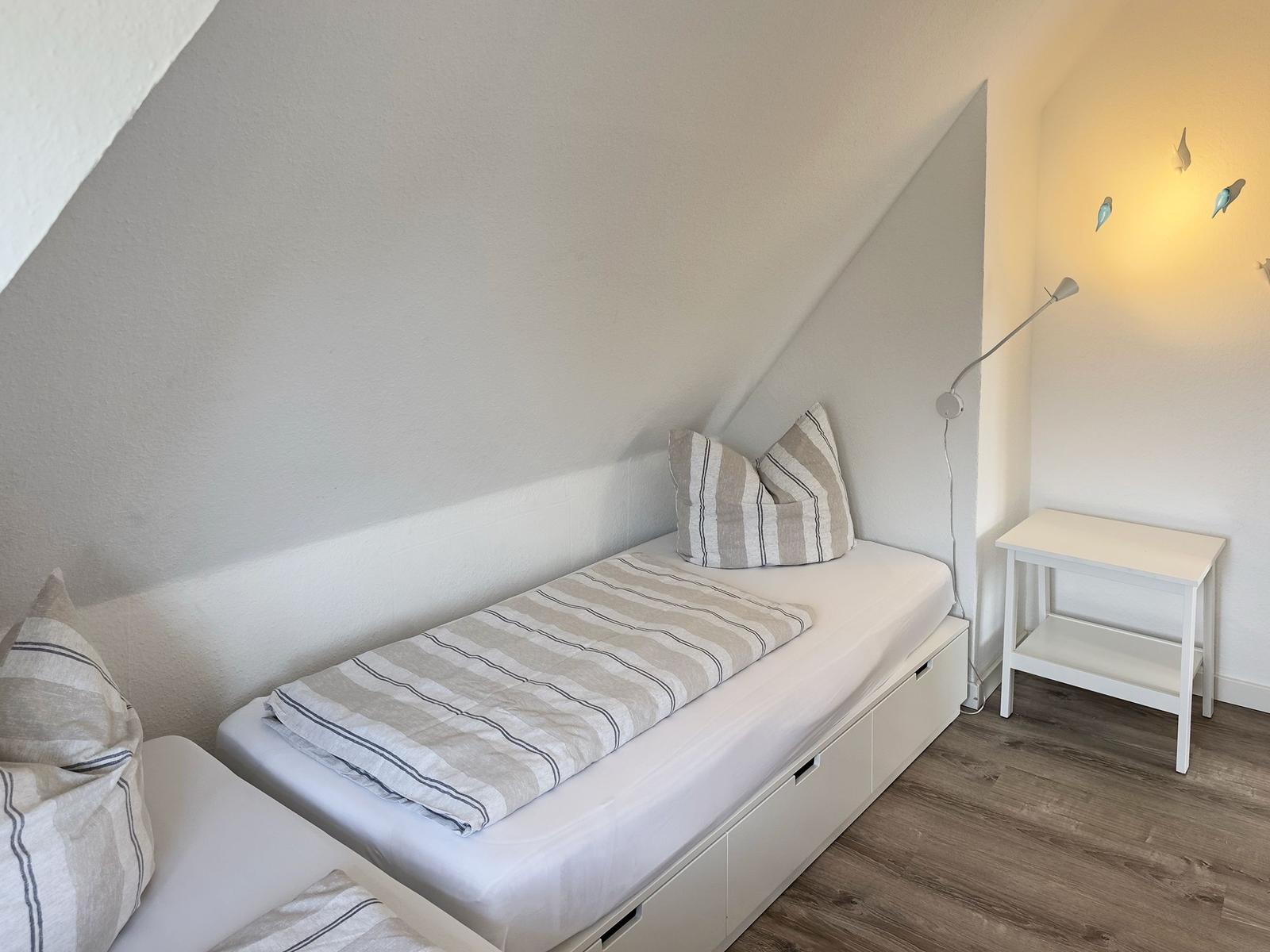 Schlafzimmer mit Dachschrägen, Bett mit Kissen und Nachttisch.