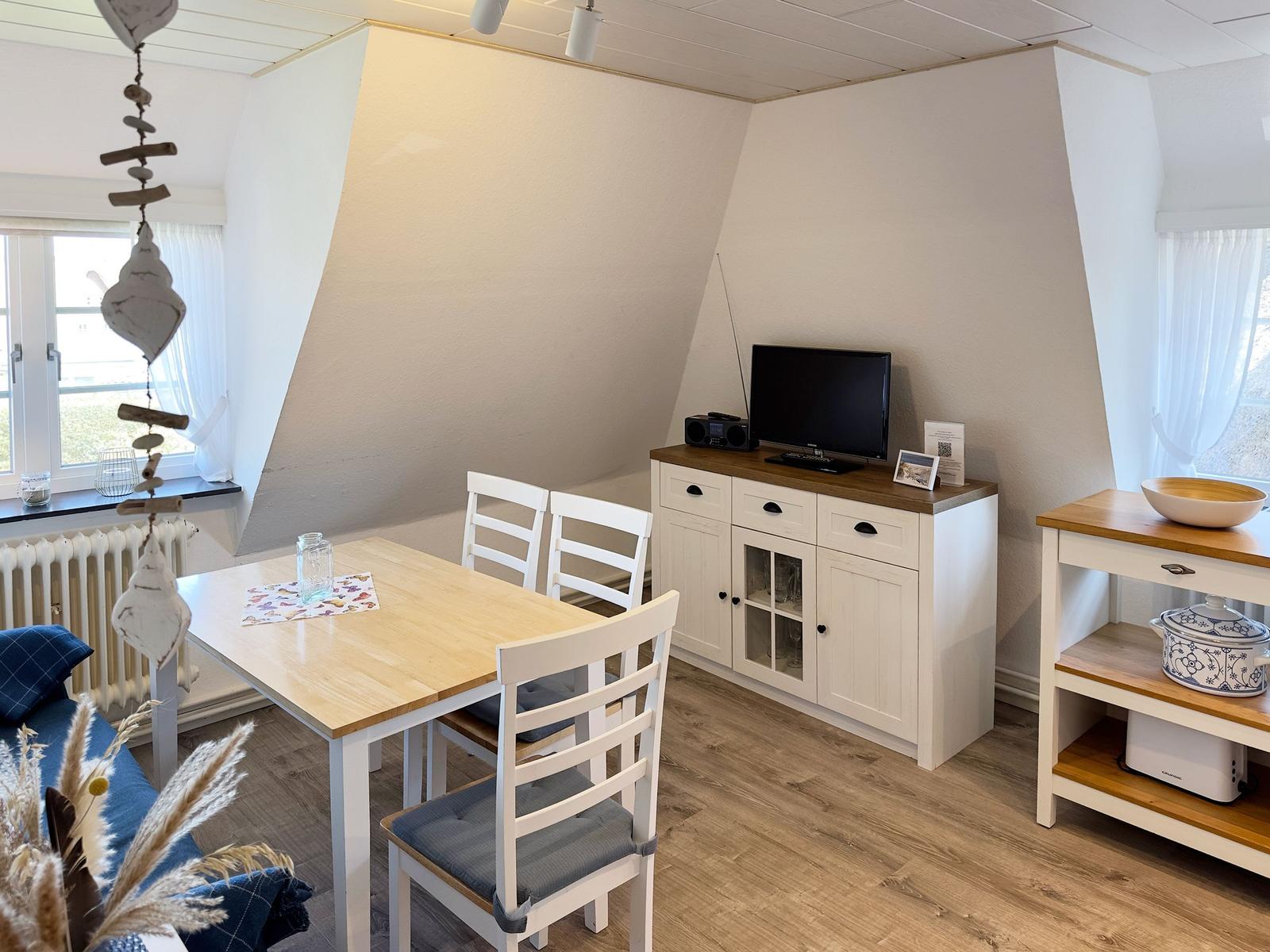 Esszimmer mit Tisch, Stühlen, Fernseher und Küchenmöbeln.