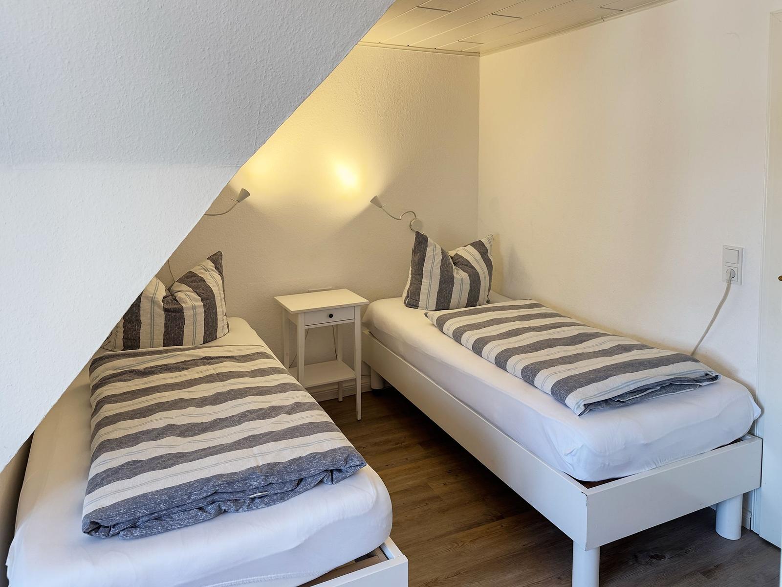 Zwei Einzelbetten unter Dachschräge mit Nachttisch und Wandlampen.