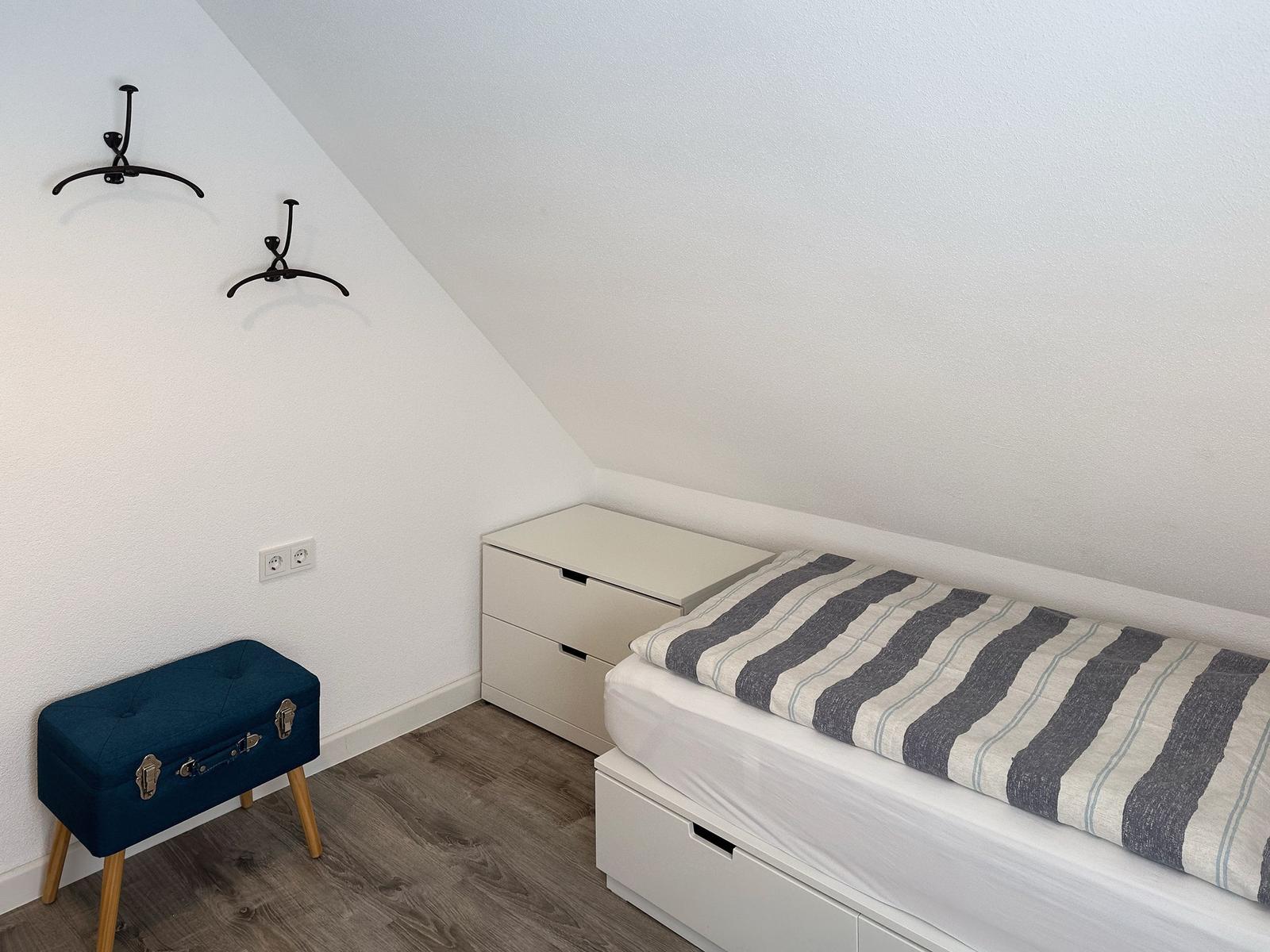 Bedroom with sloped ceiling, bed, nightstand, and blue stool.