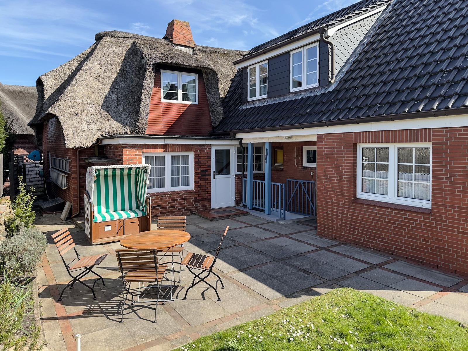 House with thatched roof, terrace with garden furniture and green lawn.