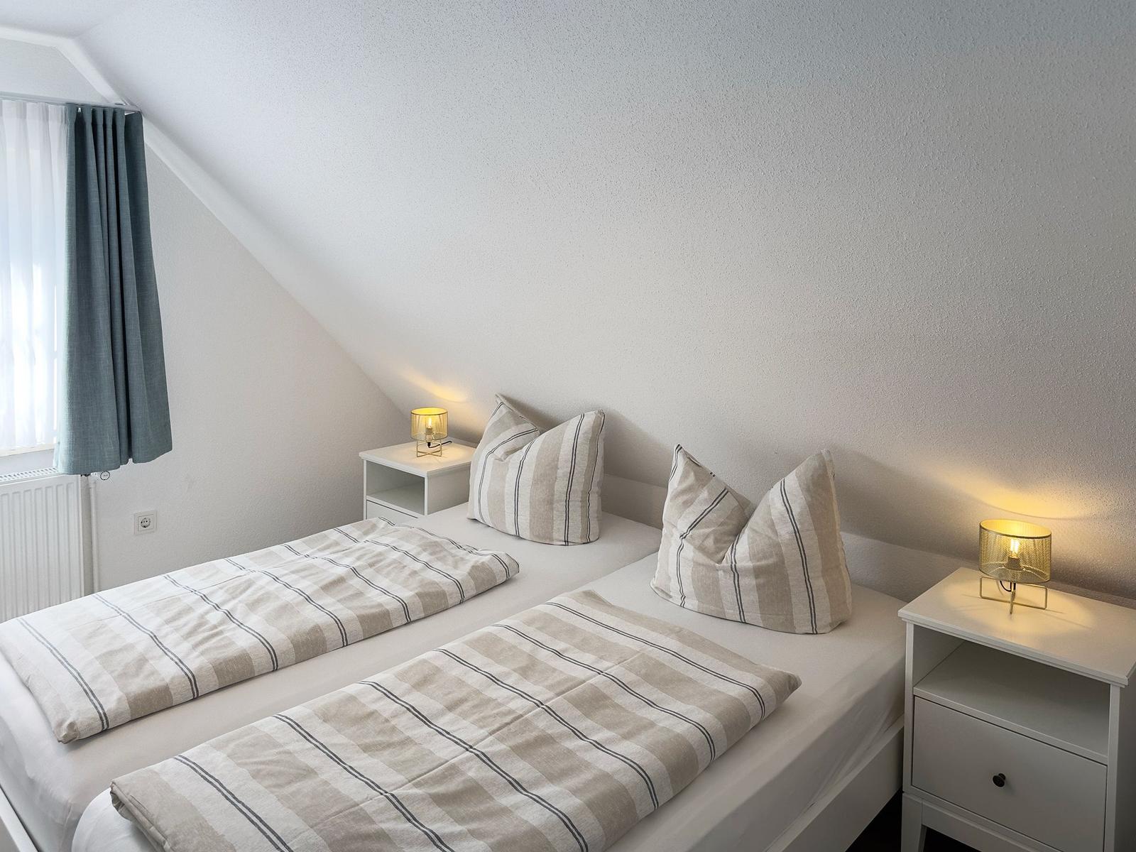 Room with double bed, two nightstands and lamp. Window with curtains.