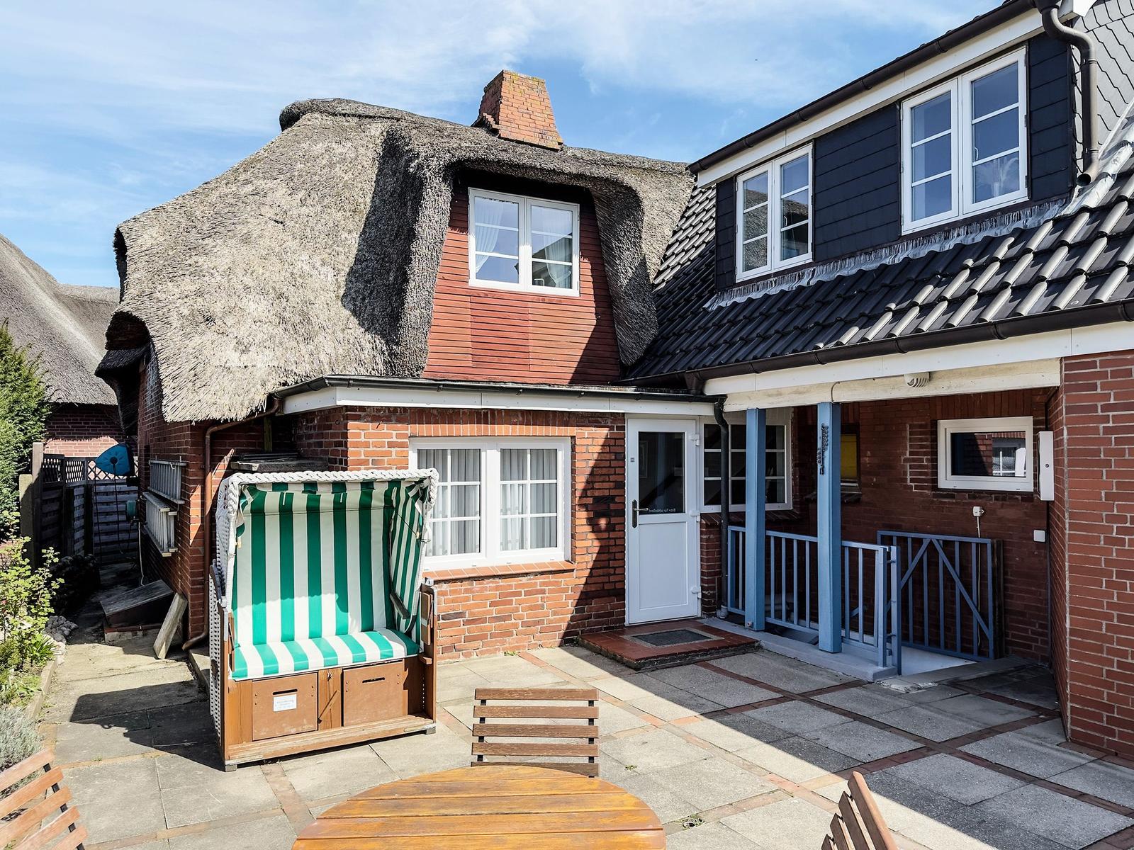 House with thatched roof, terrace, and beach chair. Entrance with blue pillars.