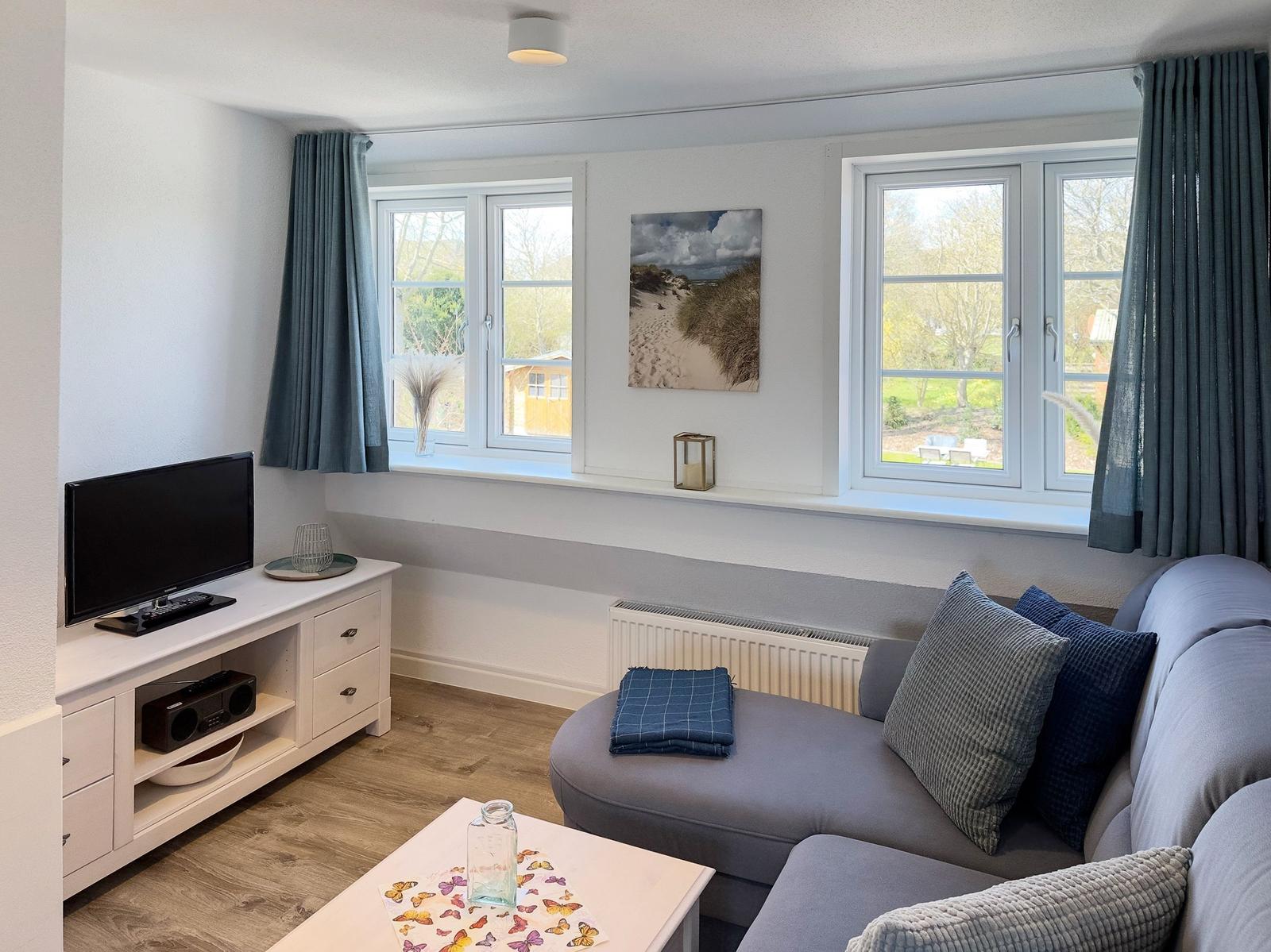 Living room with sofa, TV, and windows overlooking the garden.