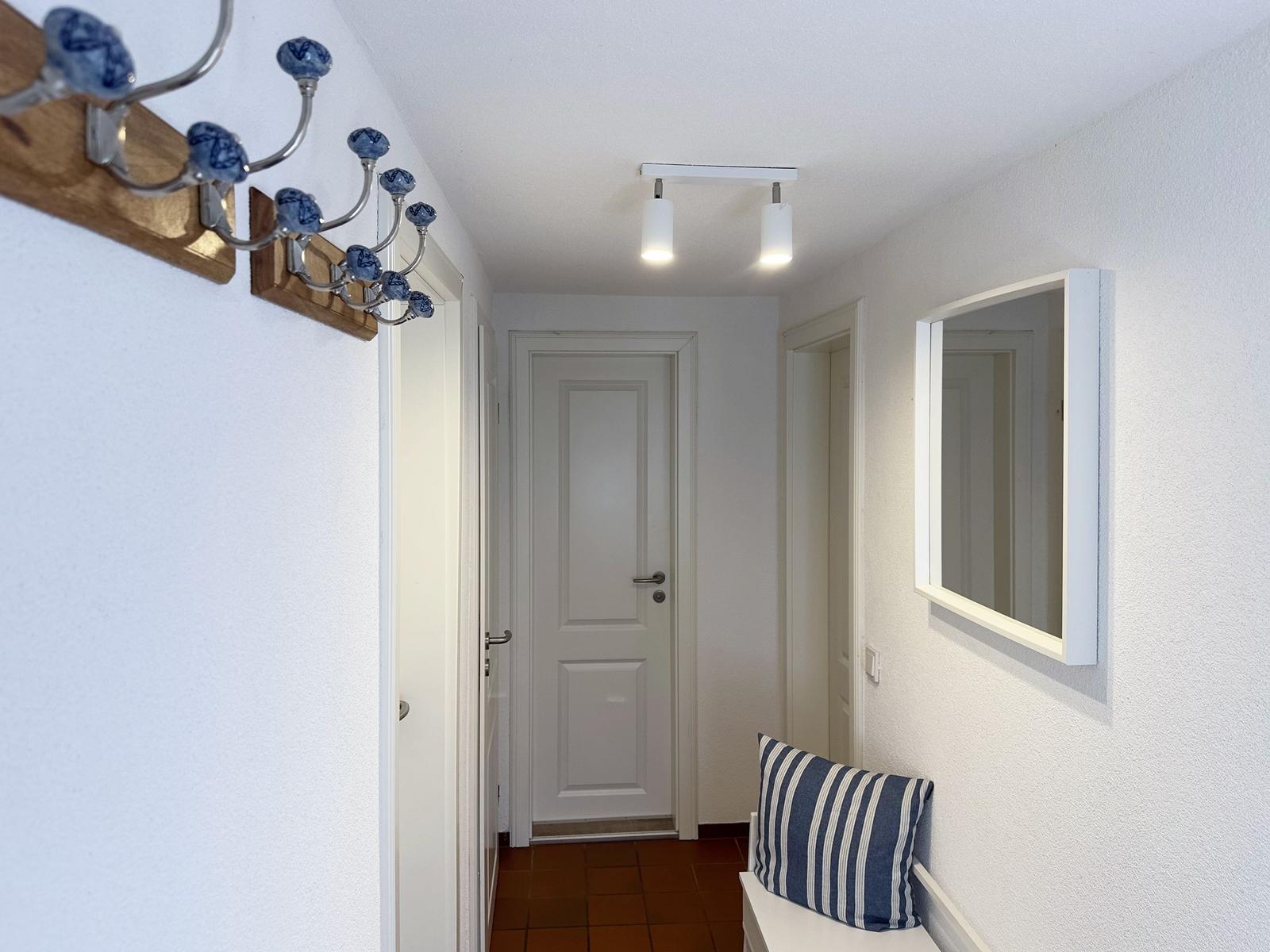 Flur mit Spiegel, Hocker und blau-weißem Kissen. An der Wand hängt ein Kleiderhaken mit blauen Kugeln.