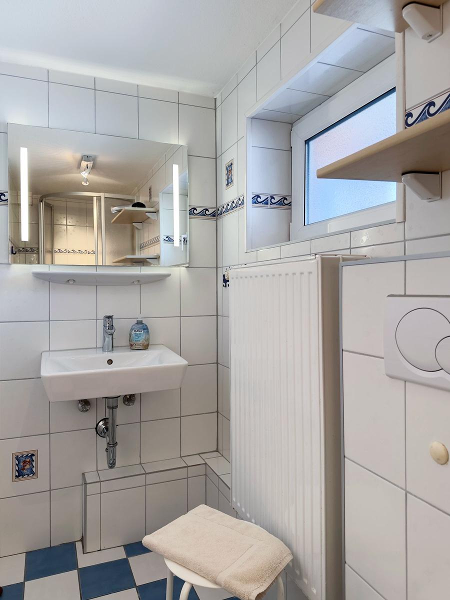 Badezimmer mit Waschbecken, Spiegel, Heizung und Fenster.