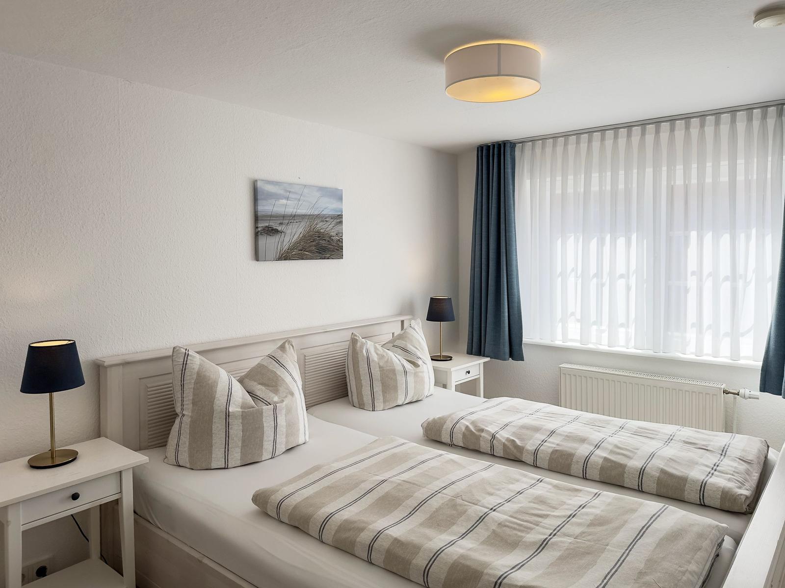 Zimmer mit Doppelbett, zwei Nachttischen und Fenster mit Vorhängen.