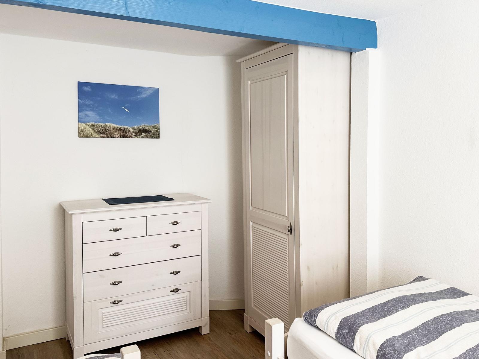 Schlafzimmer mit weißem Schrank, Schrank und Bett mit Streifenbezug.
