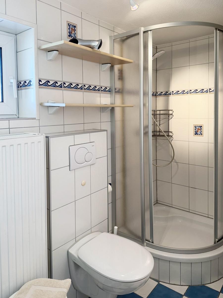 Badezimmer mit Dusche, Toilette und Fenster. Fliesen mit Wellenmuster.