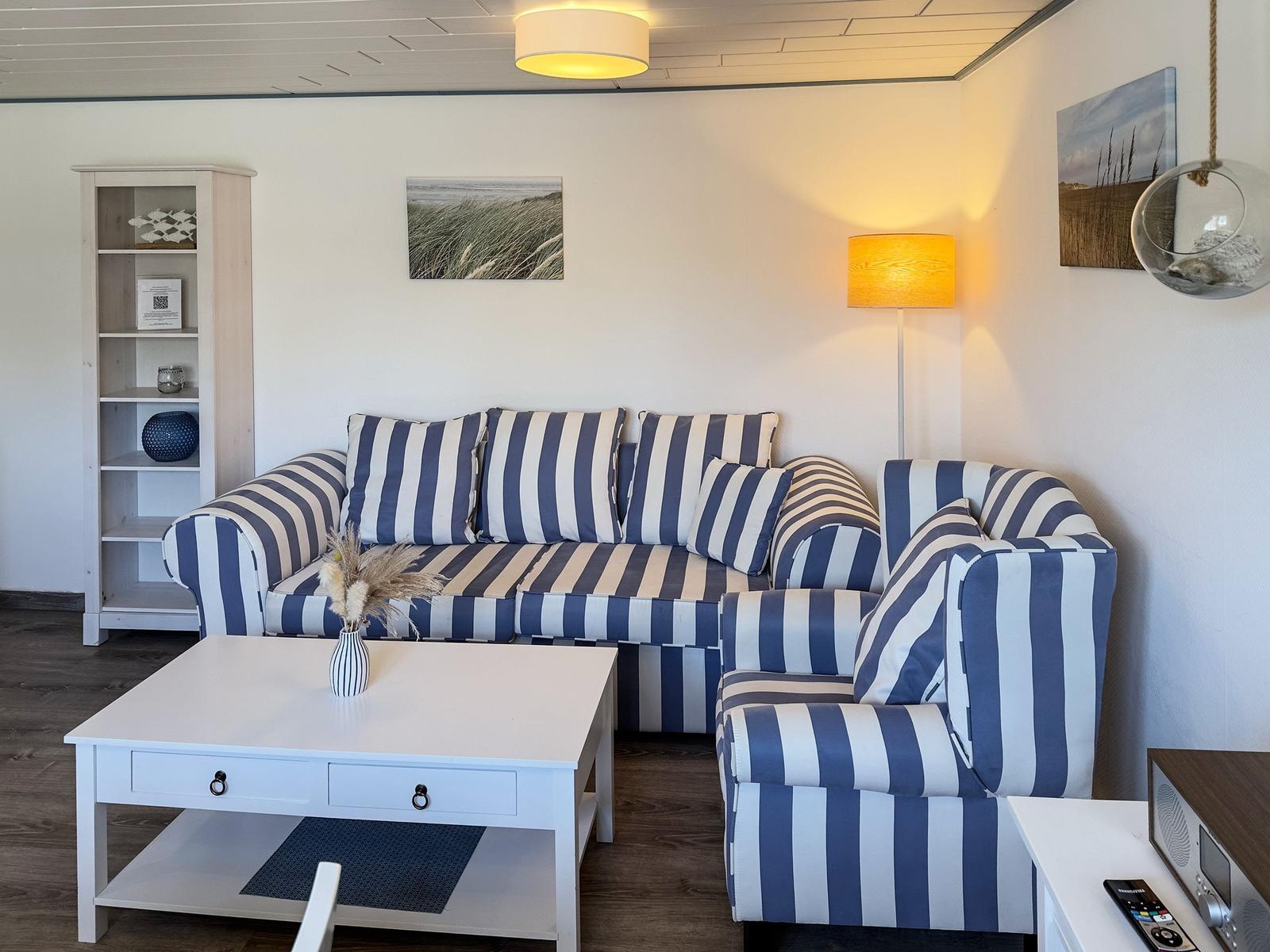Wohnzimmer mit gestreiftem Sofa, weißen Möbeln und Wandbildern.