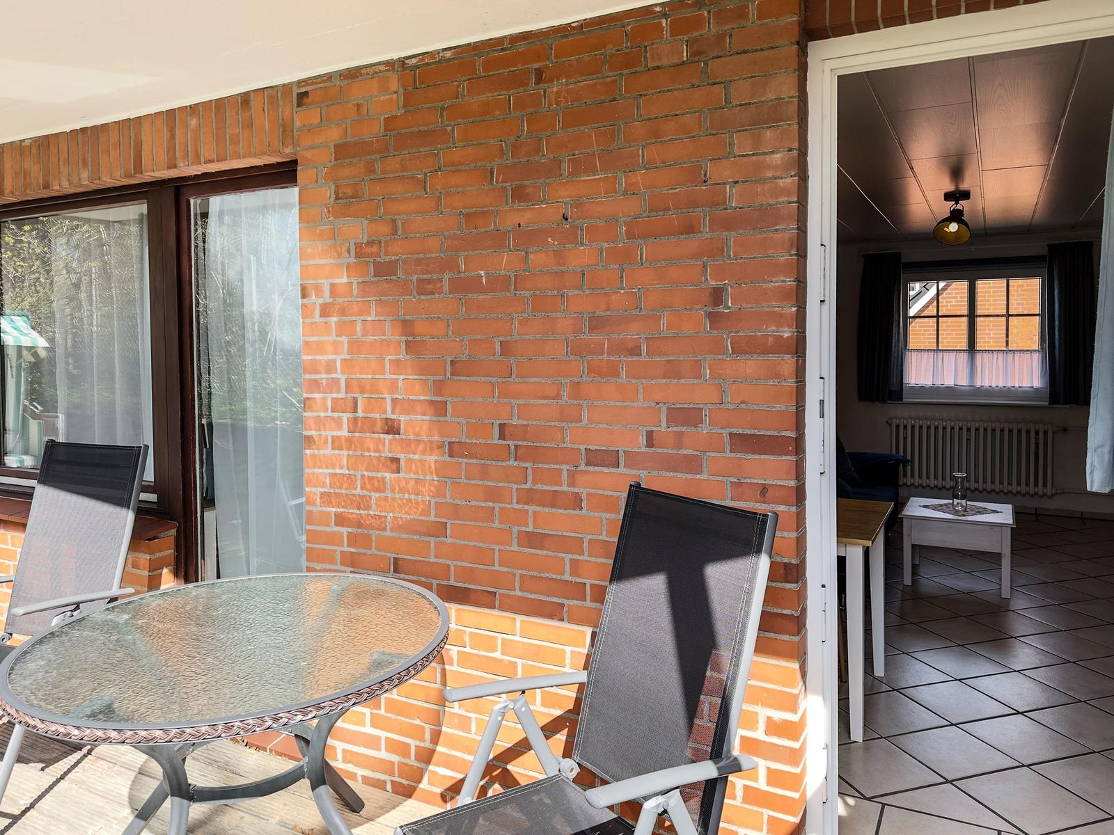 Terrace with table and chairs next to living room with window and radiator.