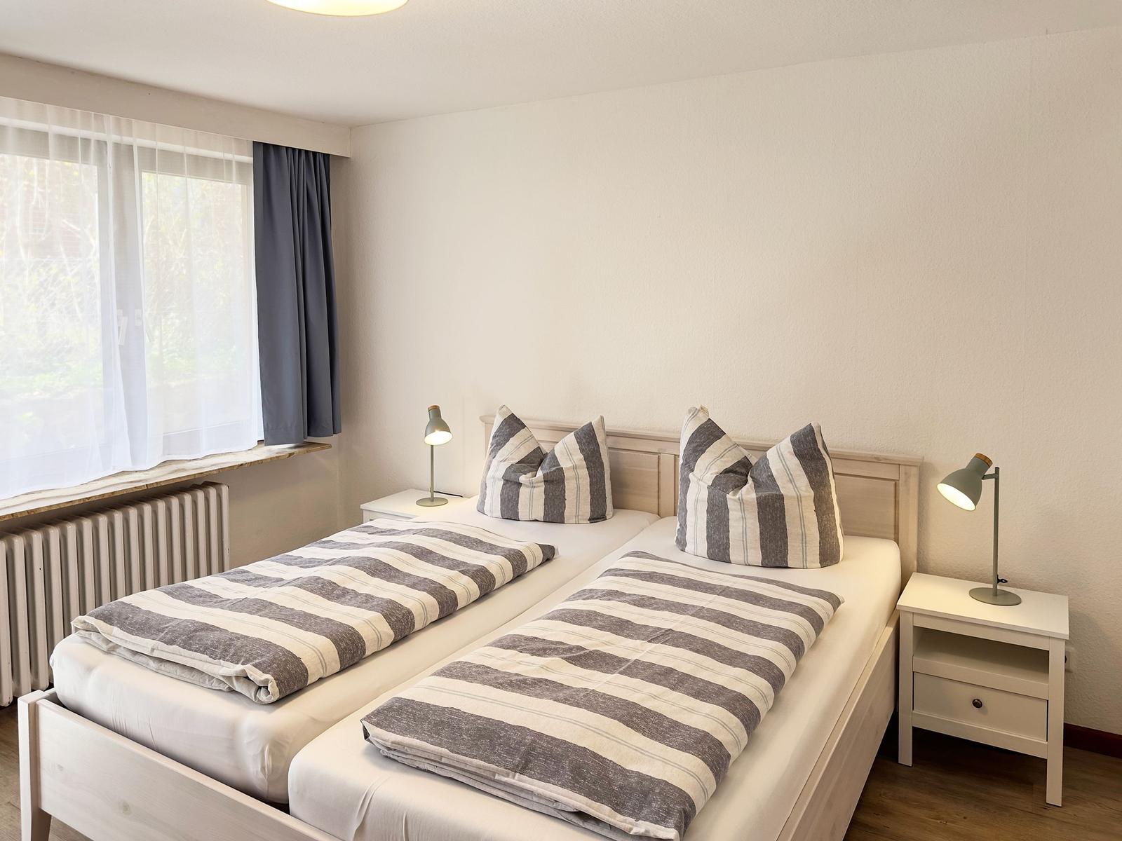 Room with two single beds, window, nightstands, and lamps.