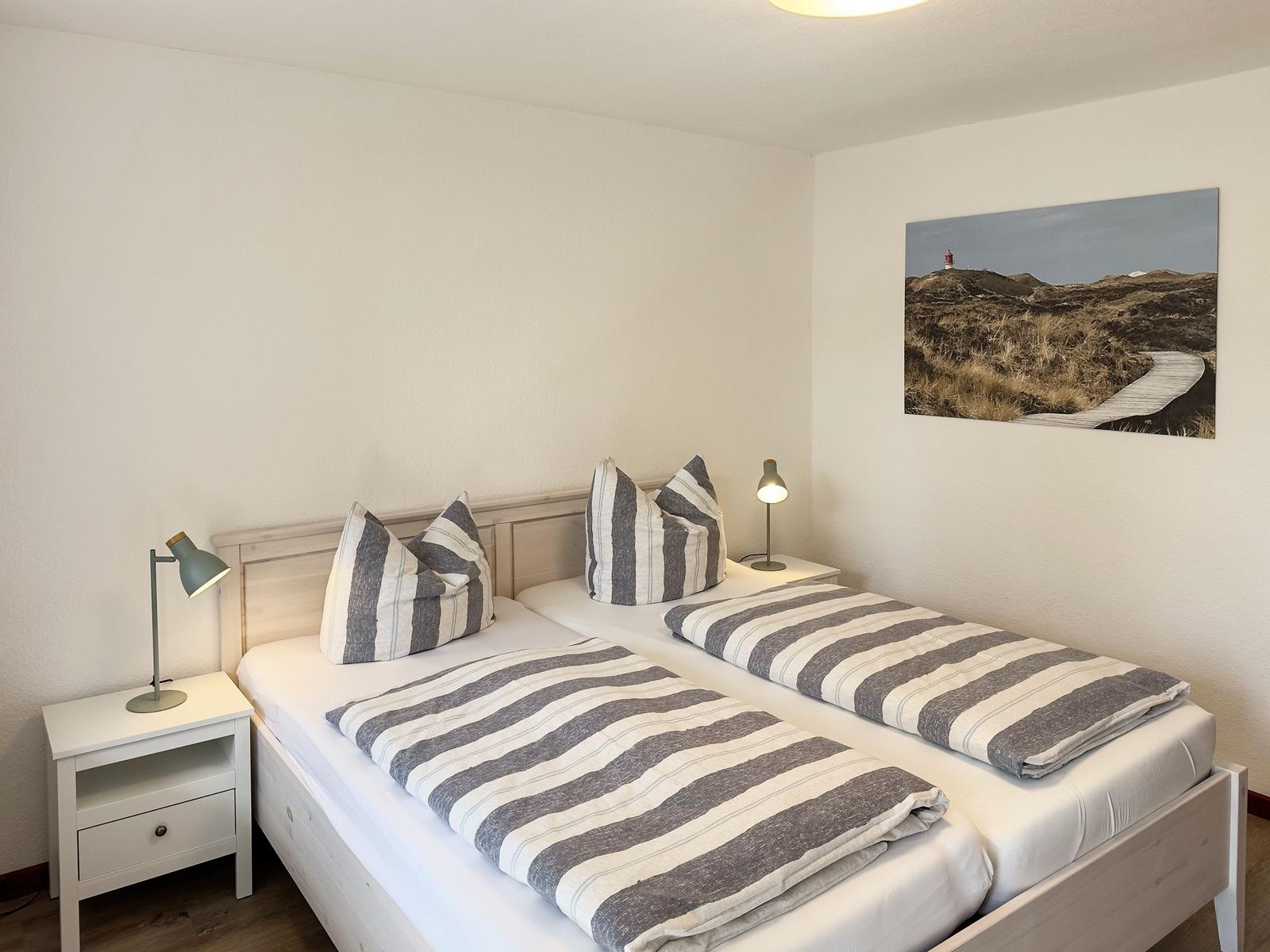 Two single beds with striped covers, nightstands, and wall art with lighthouse.